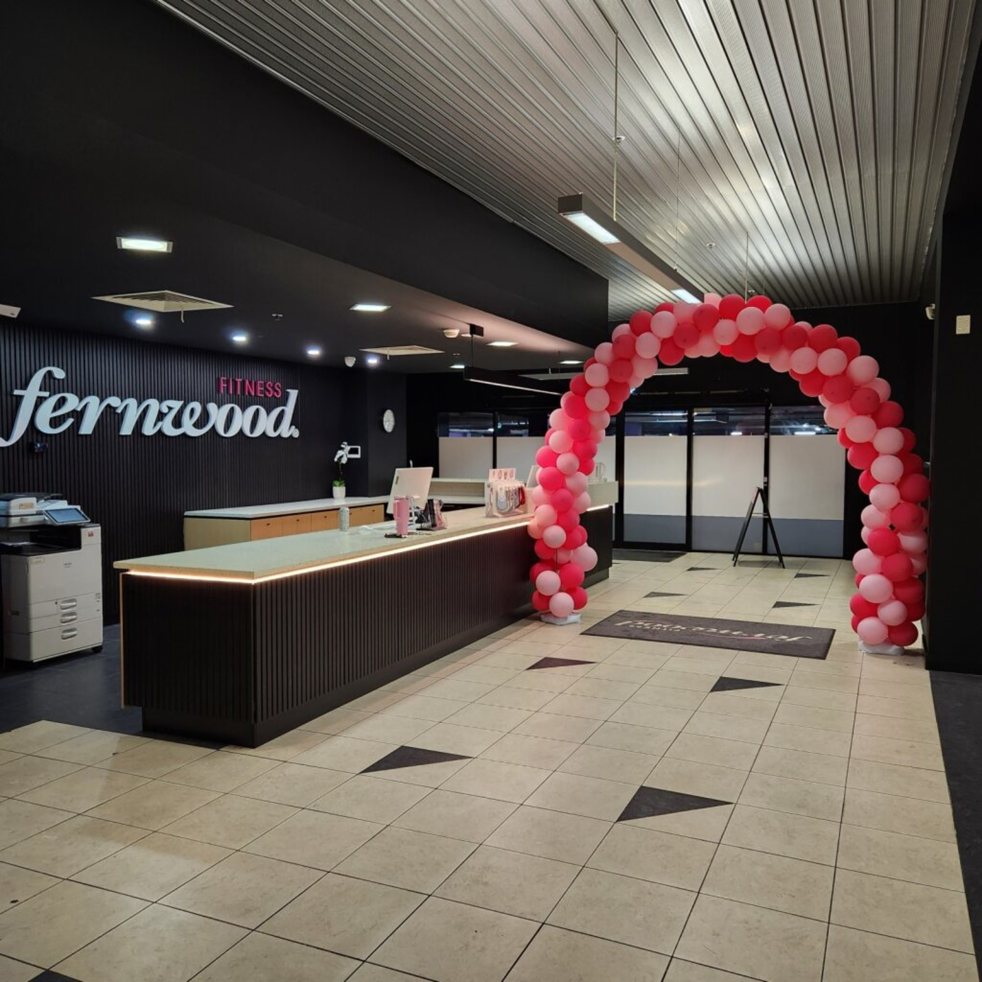 Indoor reception-style entrance with a pink and white balloon arch framing a modern front desk area.