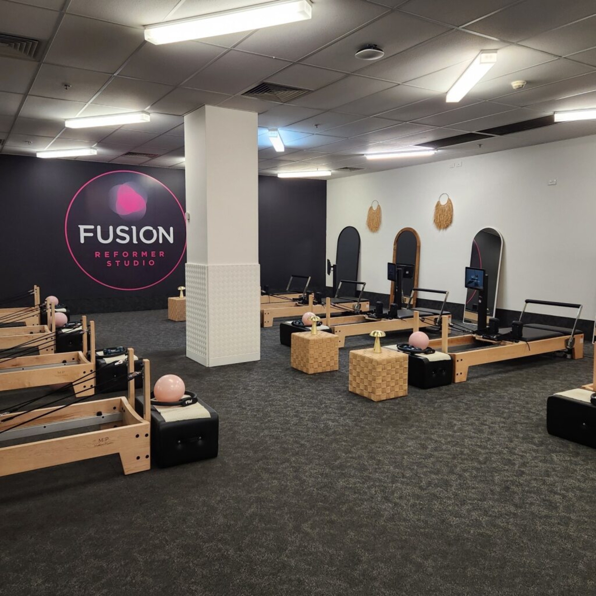 Modern pilates reformer studio interior with multiple wooden machines and a large Fusion Reformer Studio wall logo.