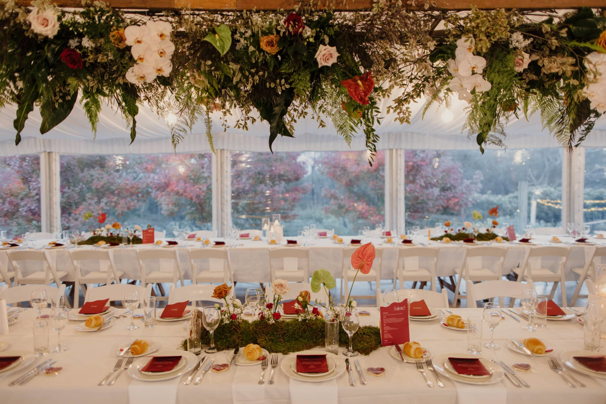 Elegant wedding reception tables with hanging greenery and floral arrangements in a light-filled marquee.