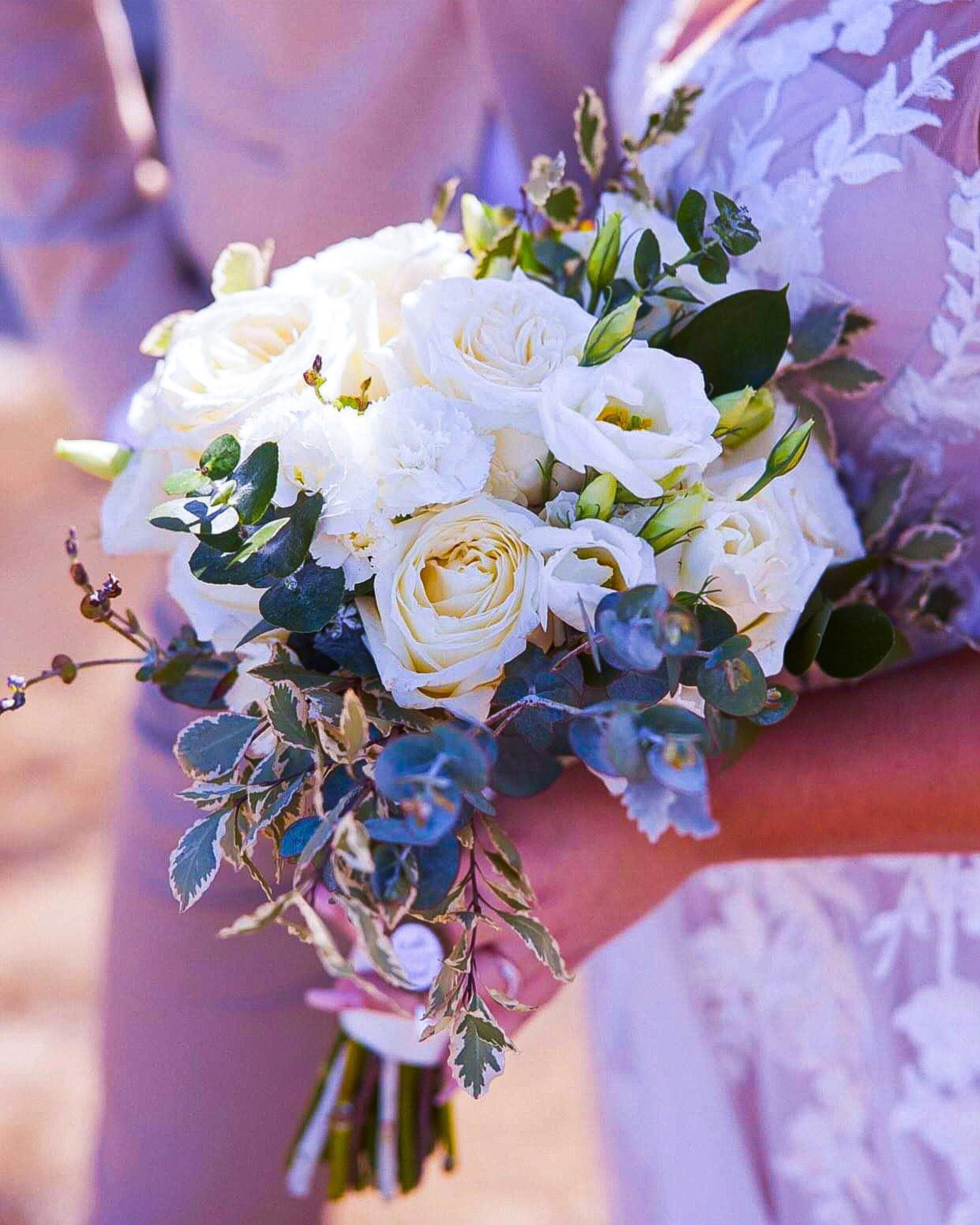 Bride holding a romantic white rose and eucalyptus bouquet with lace wedding dress details visible.