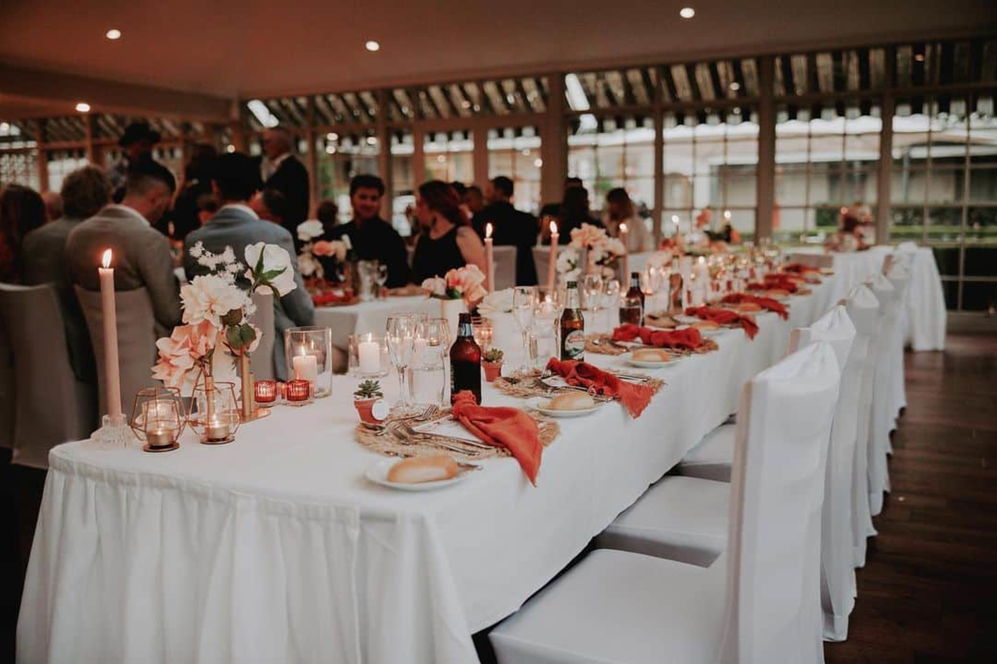 Candlelit wedding reception with long banquet tables decorated with flowers, linen napkins, and place settings.