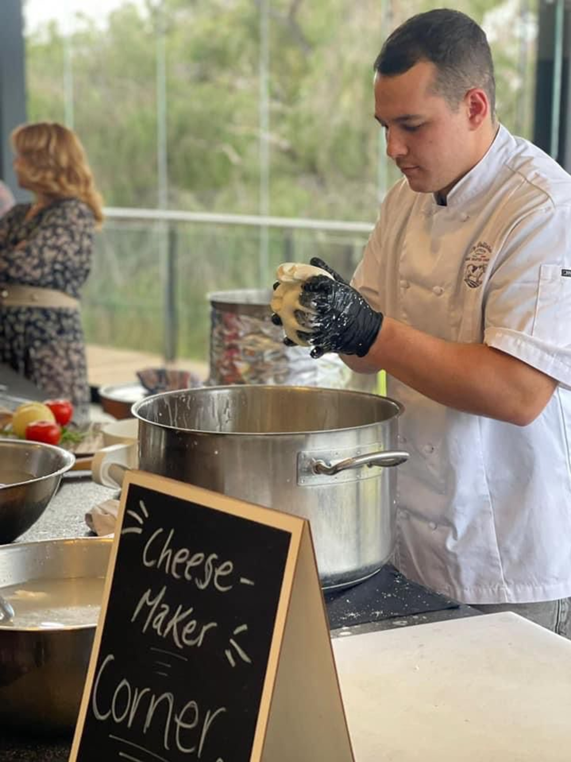 Chef prepares fresh cheese at a wedding catering cheese-maker corner with large pots and a display sign.