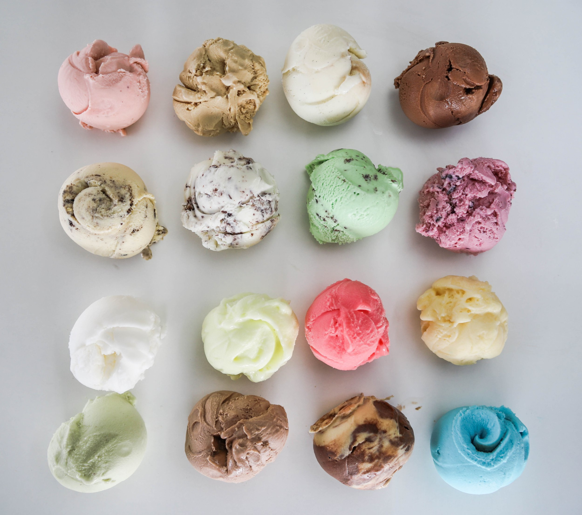 Assorted colorful ice cream scoops arranged in a neat grid on a white background.