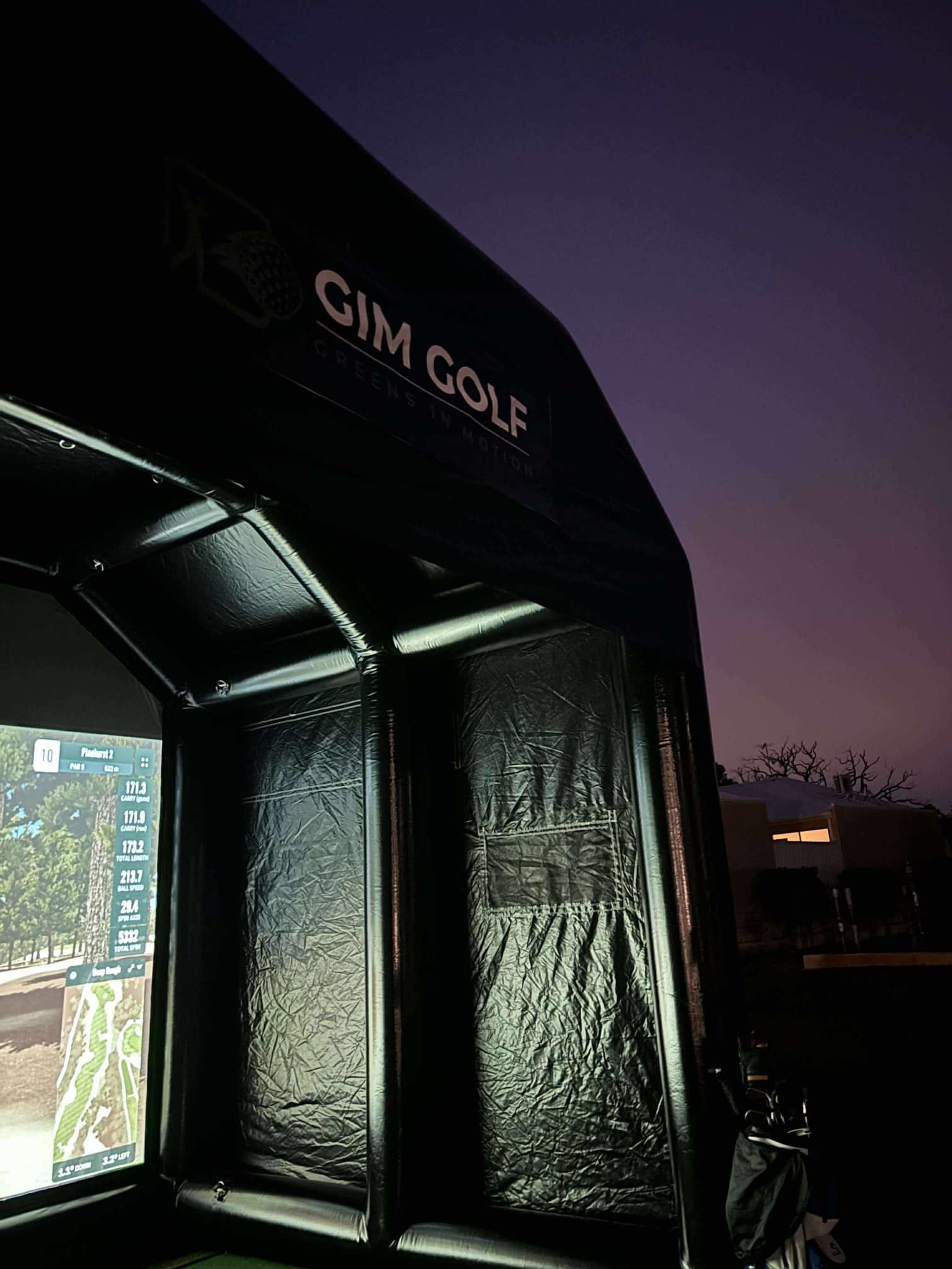 Outdoor golf simulator tent lit at night with a projected course screen.