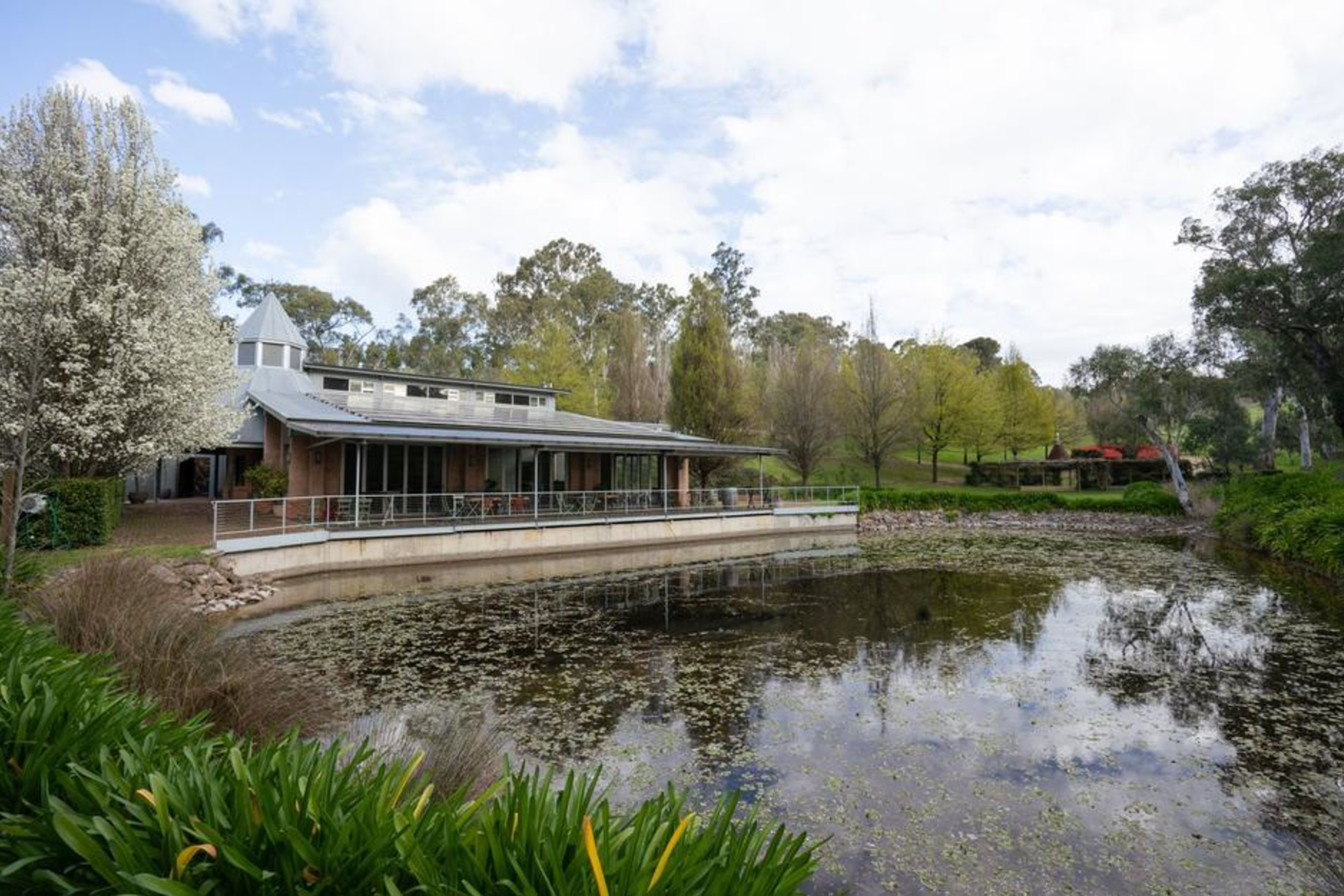 Lakeside wedding venue with modern pavilion surrounded by lush trees and gardens.