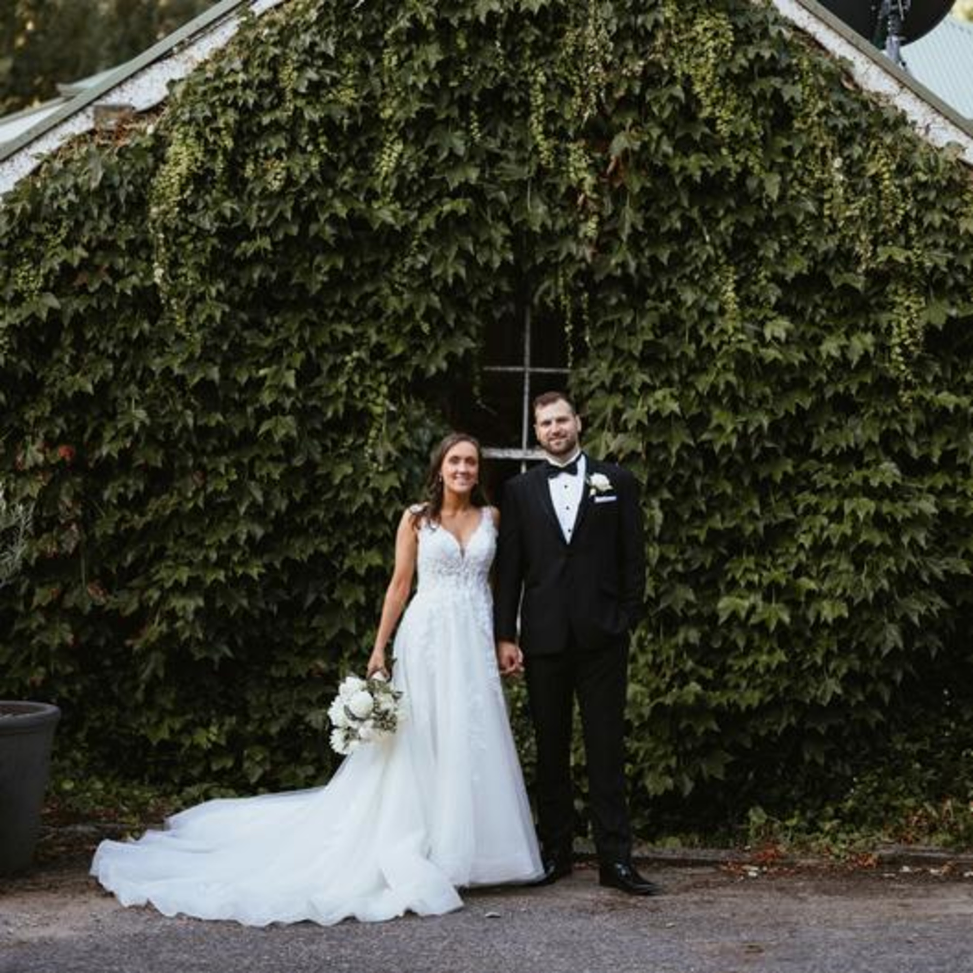 Bride and groom pose in front of an ivy-covered greenhouse wall on their wedding day