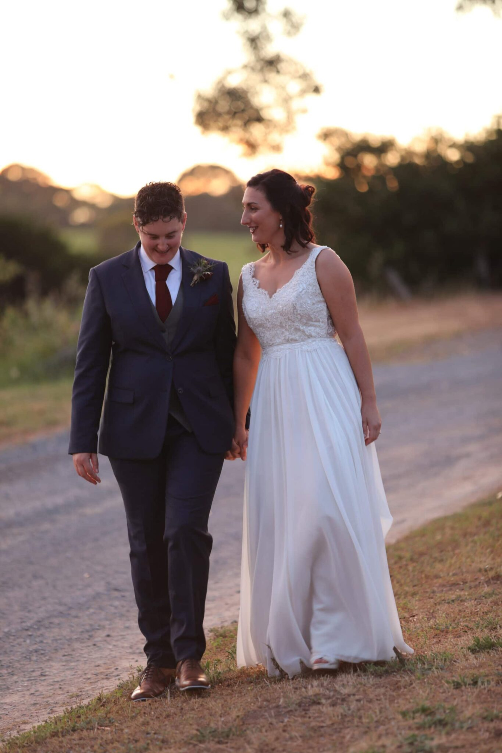 Wedding couple holding hands and walking along a country road at sunset.