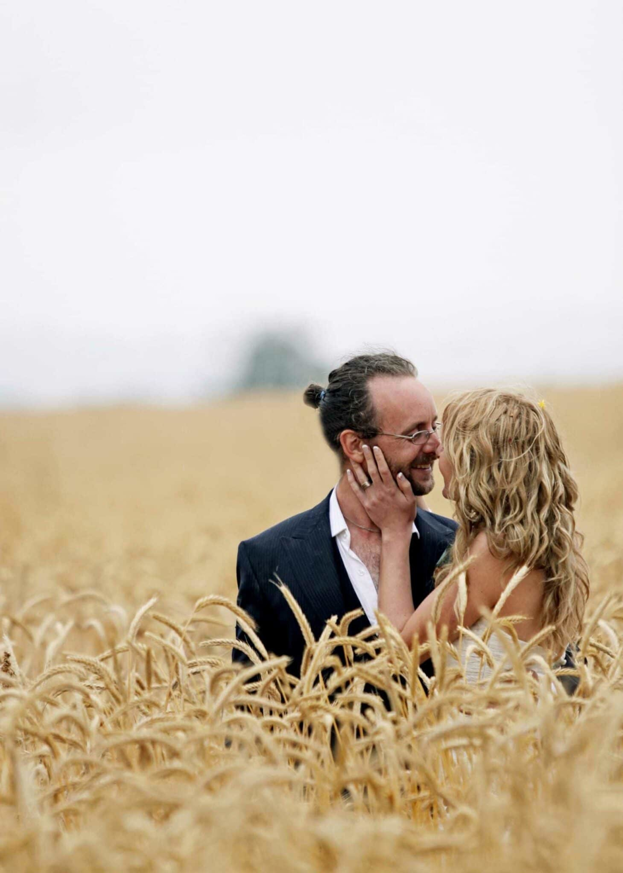 A bride and groom embrace and smile at each other while standing in a golden wheat field.