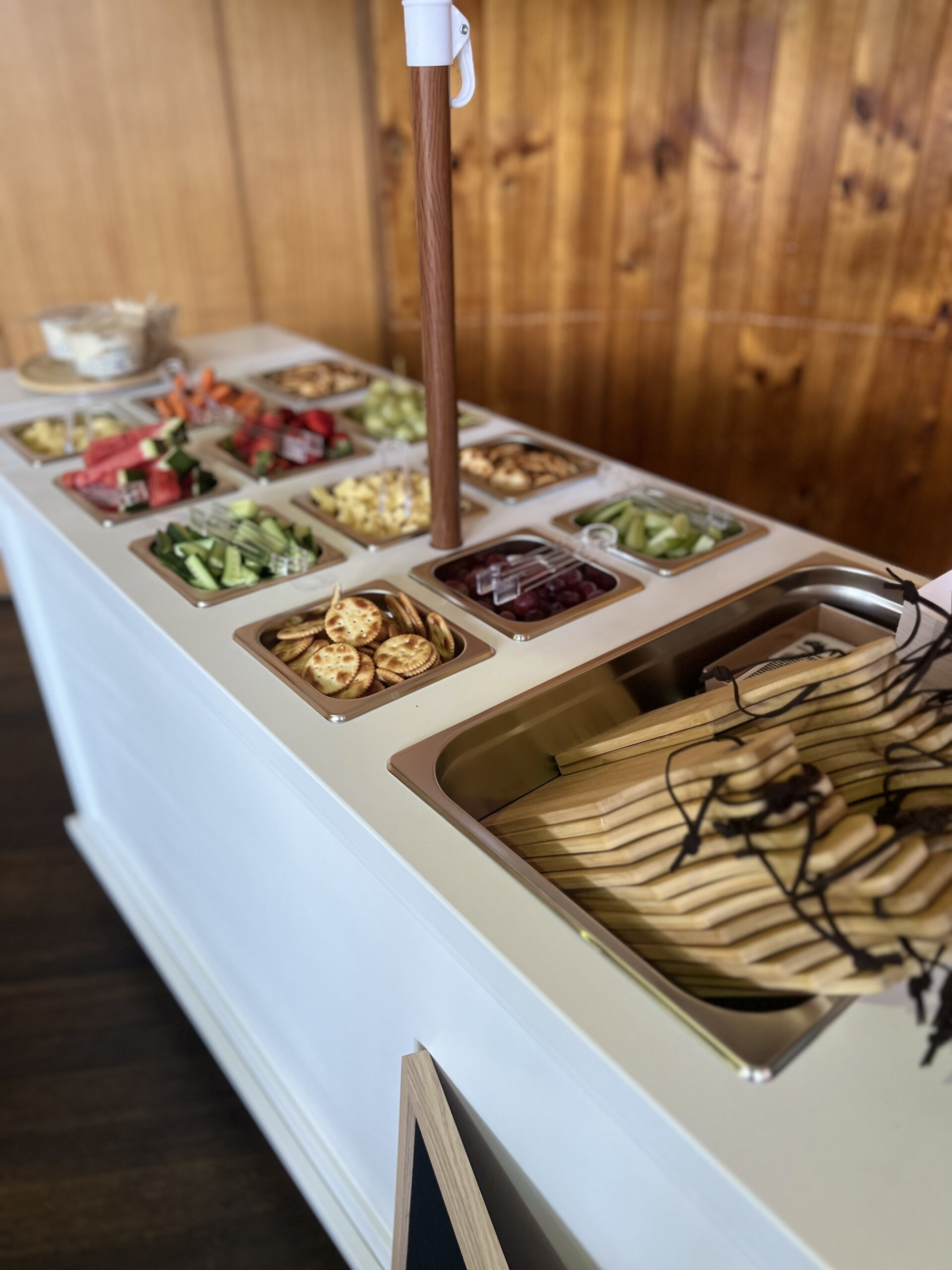 Self-serve wedding buffet station with assorted fruits, vegetables, crackers, and small serving boards.
