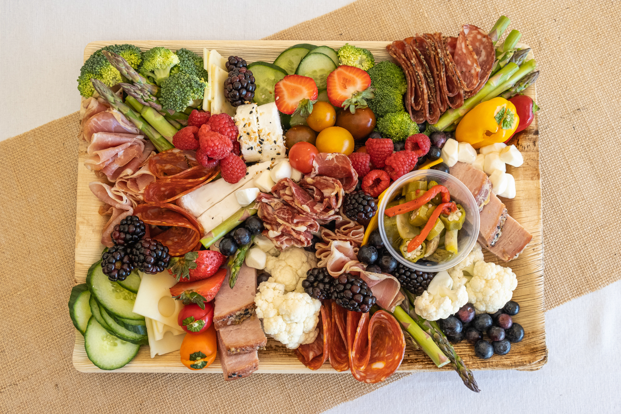 Colorful charcuterie board with meats, cheeses, fruits, and vegetables arranged on a wooden platter.