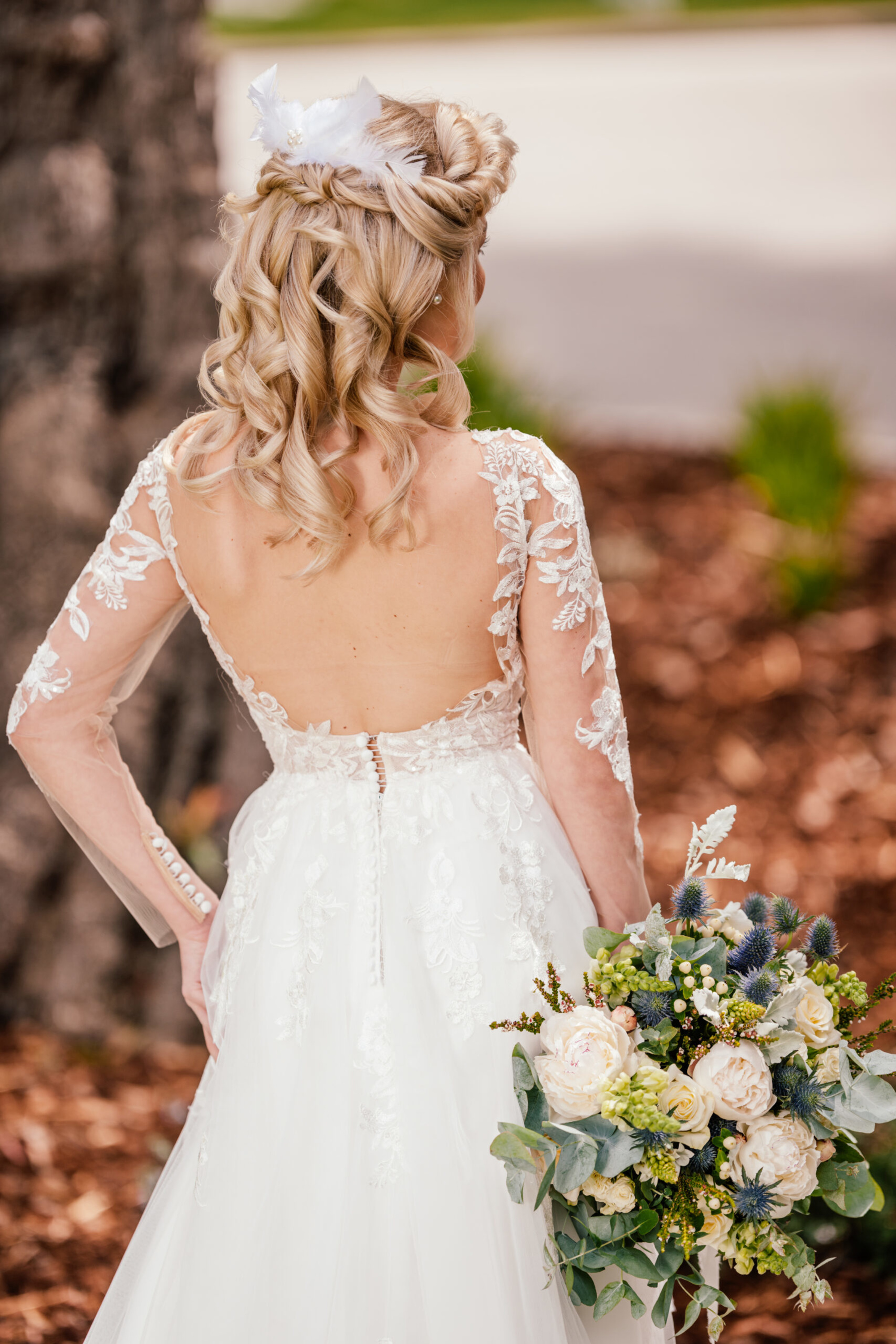 Bride in a lace open-back wedding dress holding a lush bouquet of white and green flowers outdoors.