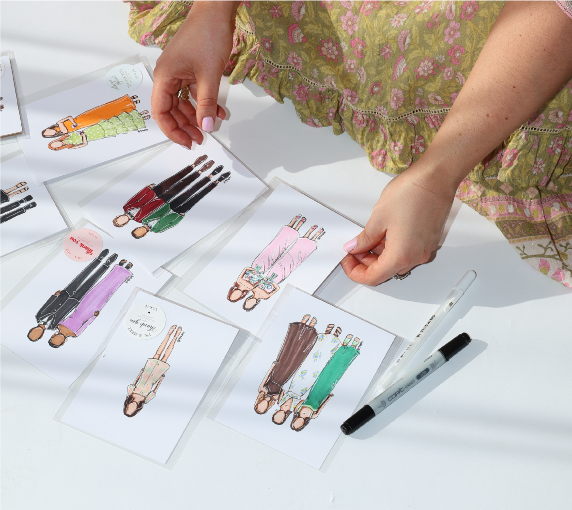 Hands arrange illustrated couple cards for custom wedding portraits on a white table.