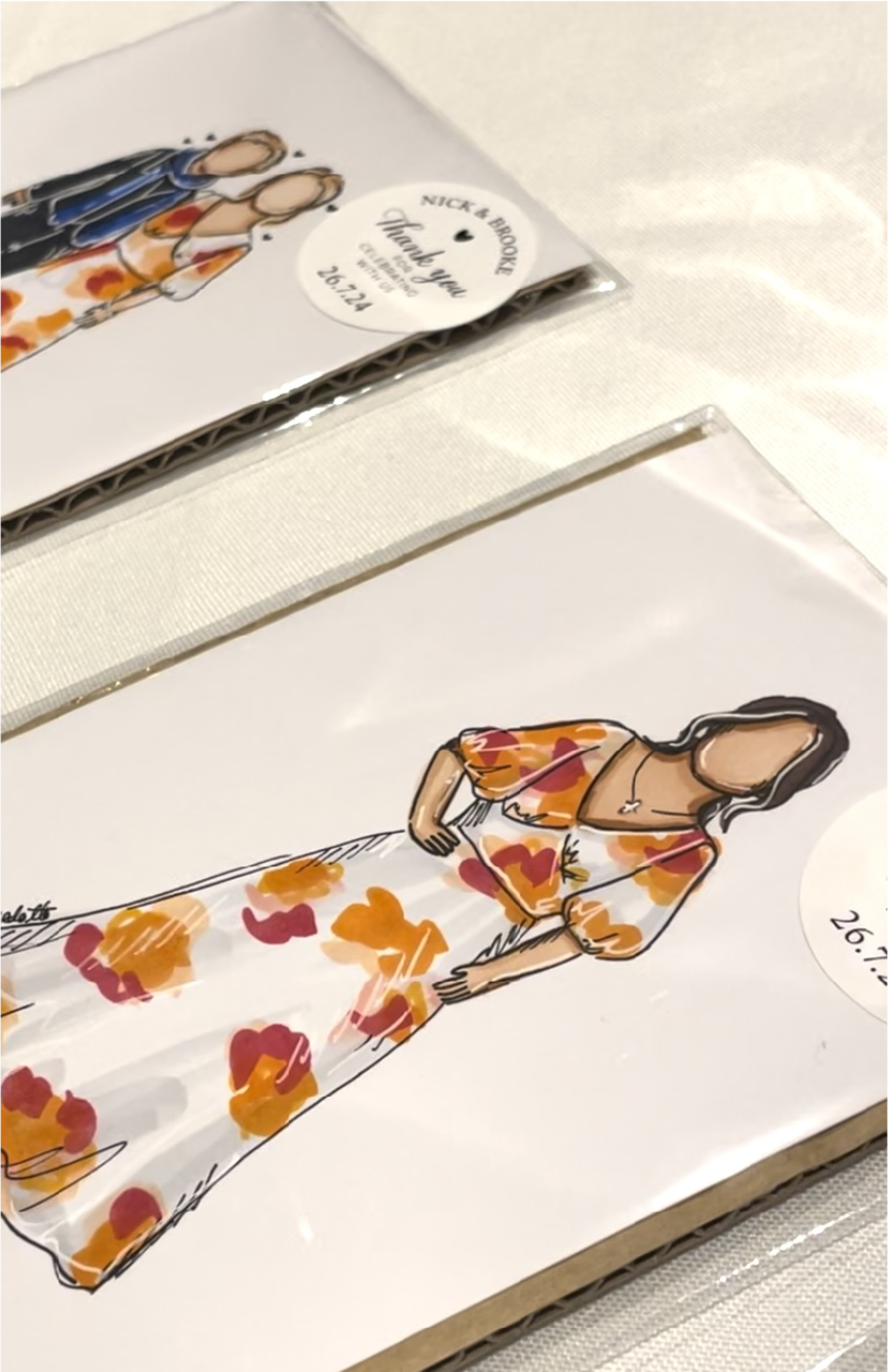Photo of custom illustrated wedding portraits used as thank you cards or favors on a light fabric surface.