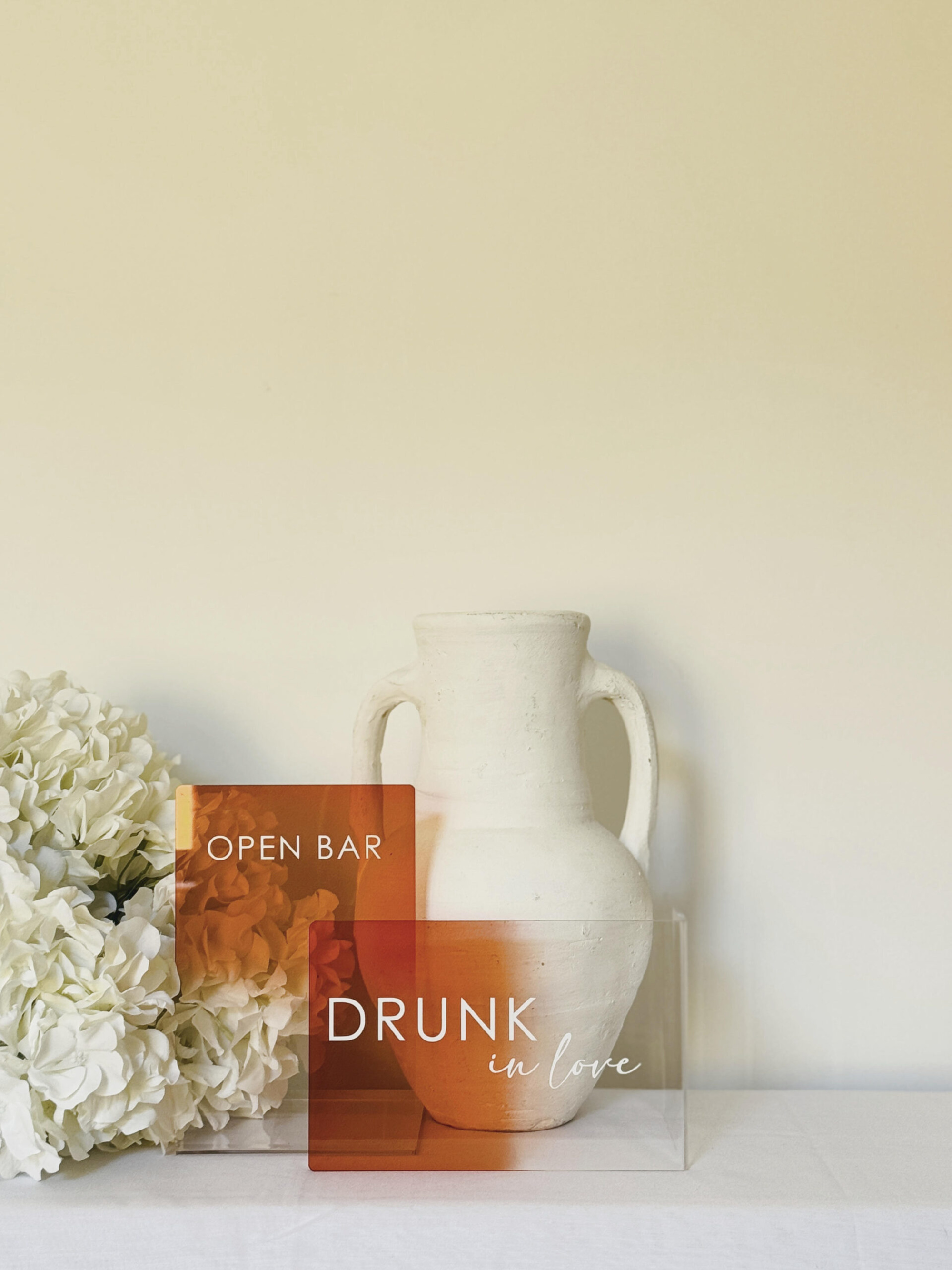 Modern acrylic wedding bar signs reading Open Bar and Drunk in Love styled with white hydrangeas and a ceramic vase.