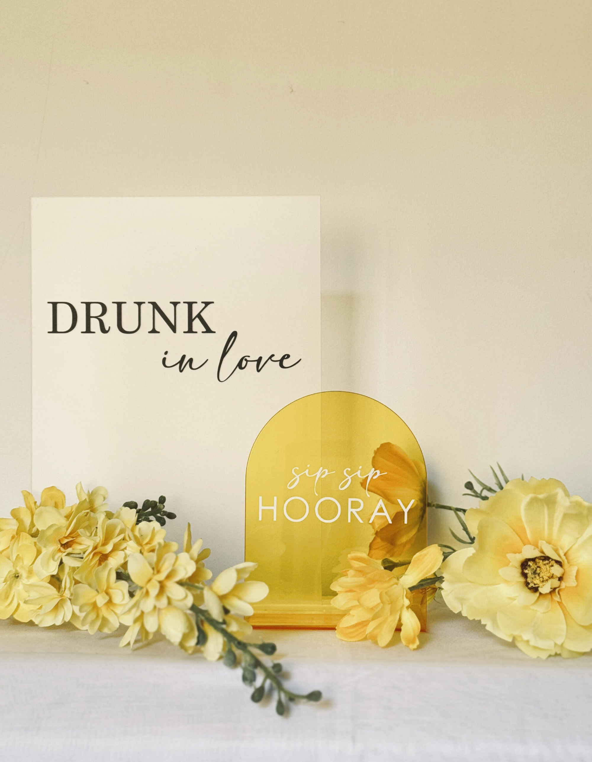 Yellow wedding bar signs reading drunk in love and sip sip hooray styled with yellow floral arrangements.