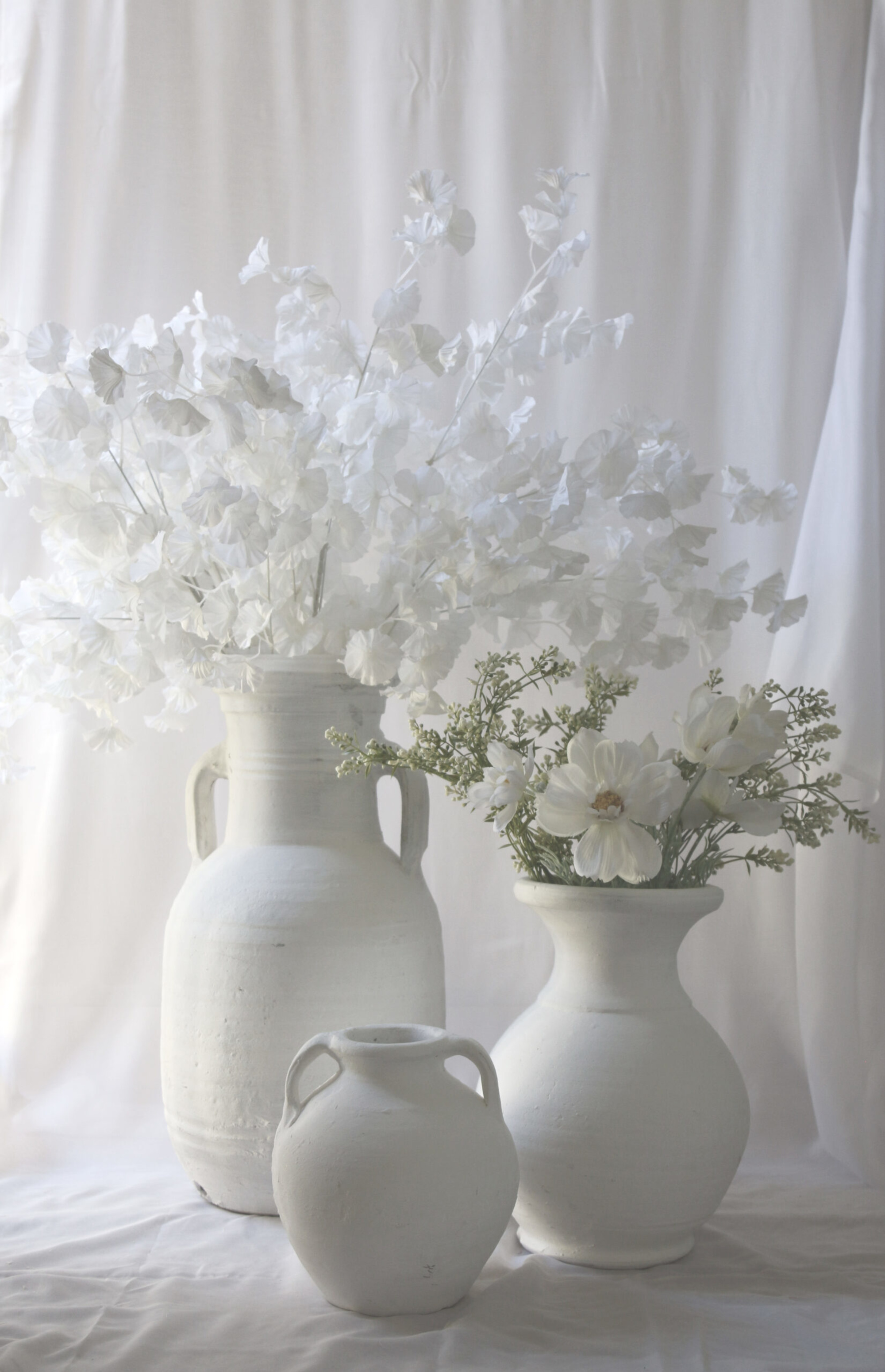 White ceramic vases filled with delicate white flowers against a soft neutral backdrop.