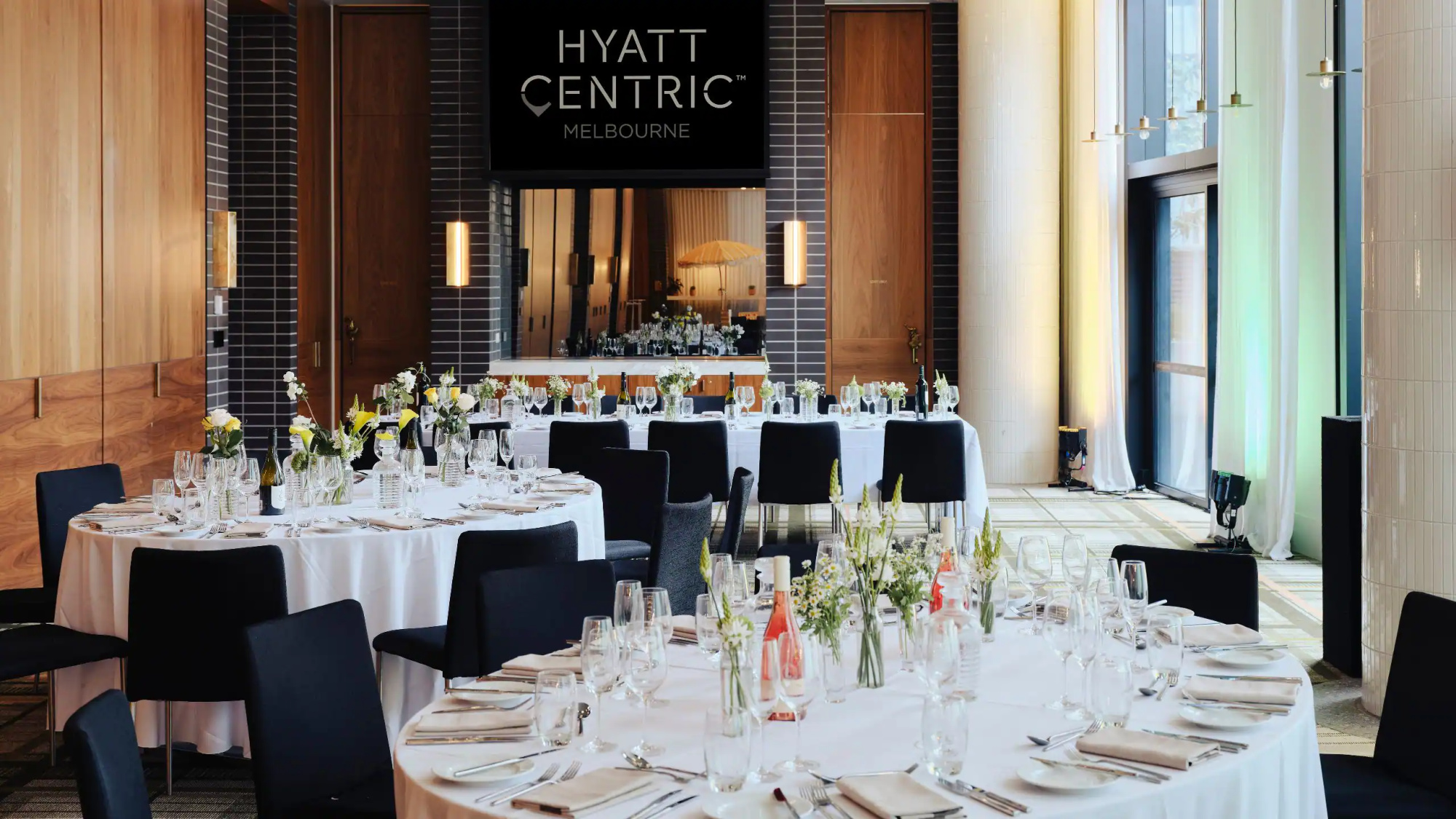 Elegant hotel ballroom in Melbourne set for a modern wedding reception with round tables and minimalist floral centerpieces.
