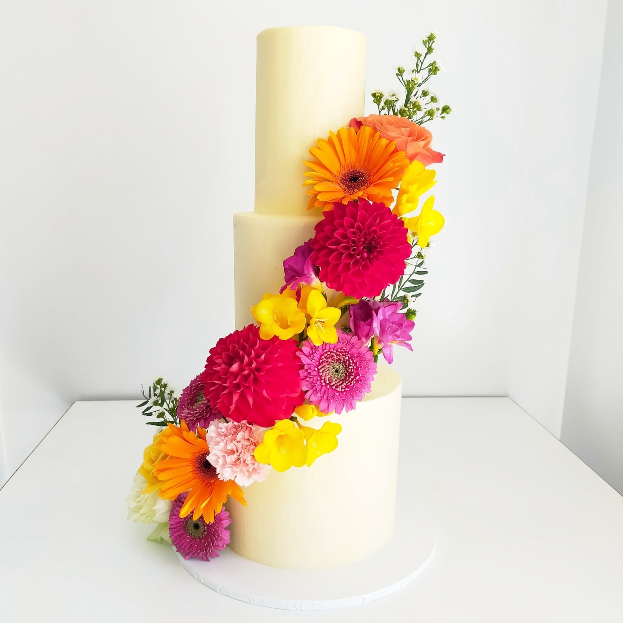 Three-tier ivory buttercream wedding cake decorated with a cascade of vibrant fresh flowers.