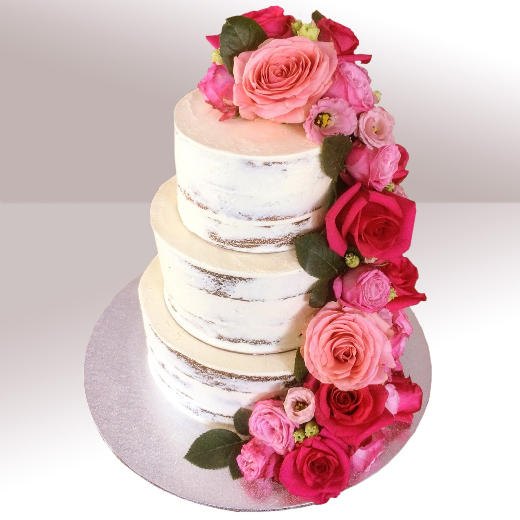 Three-tier semi-naked wedding cake decorated with cascading pink and red roses on a silver board.