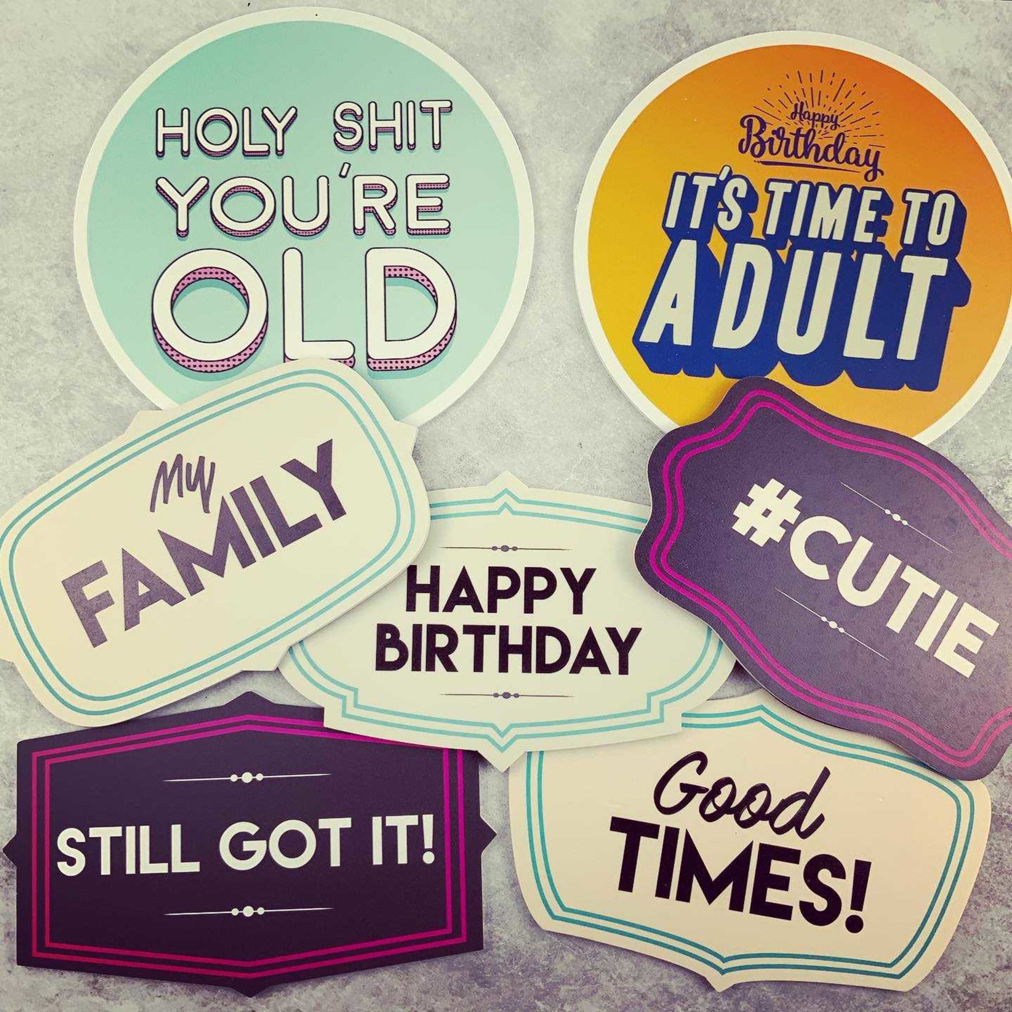 Colorful party photo booth signs with playful birthday and celebration phrases arranged on a light surface.