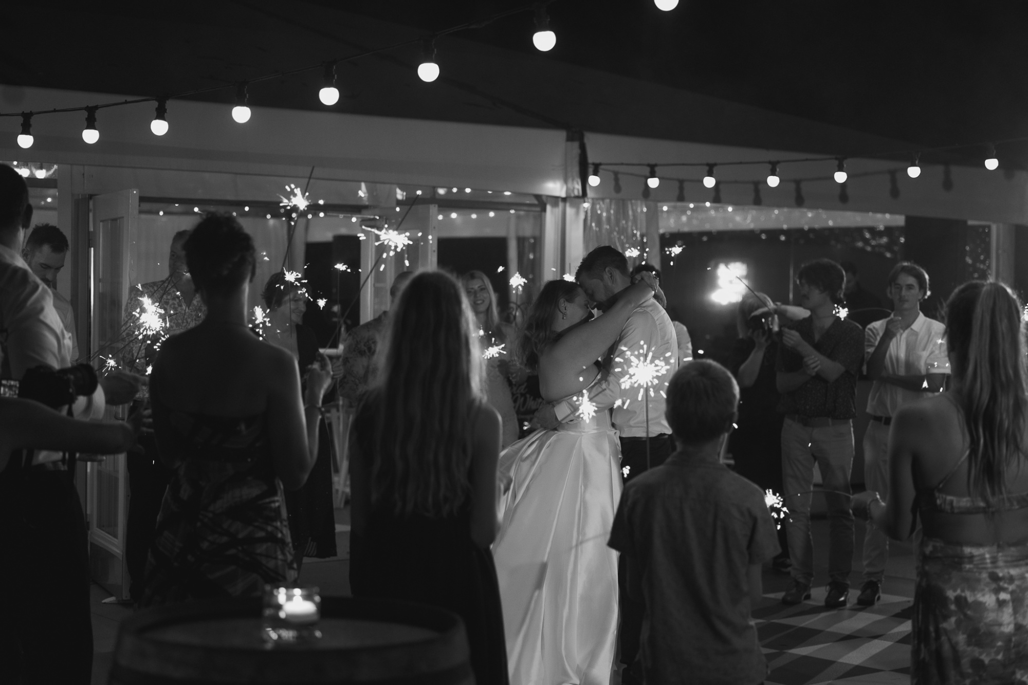 Bride and groom share a romantic dance surrounded by guests holding sparklers at an evening wedding reception.