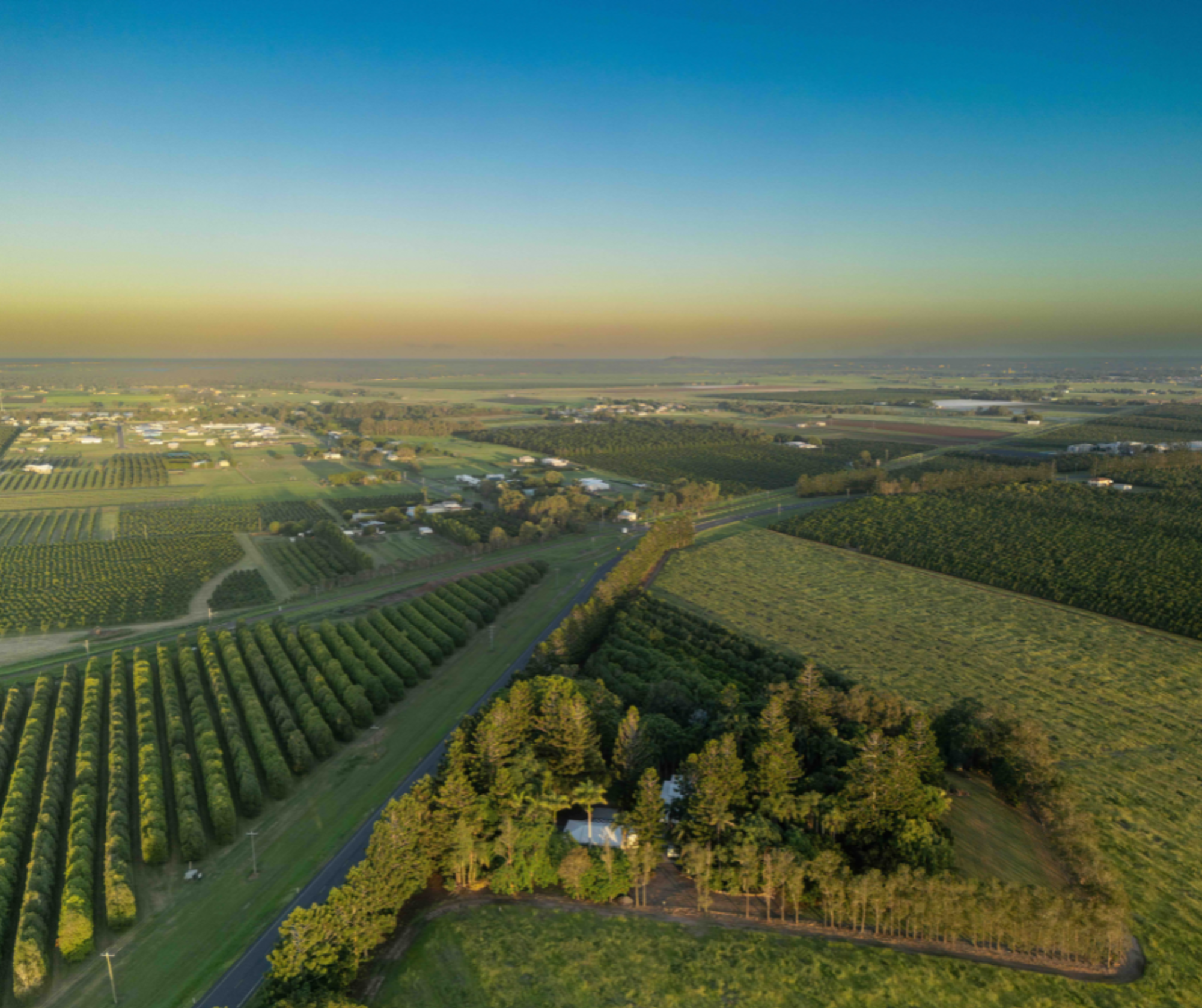 Aerial view of a rural wedding venue surrounded by expansive green fields and orchards at sunset.