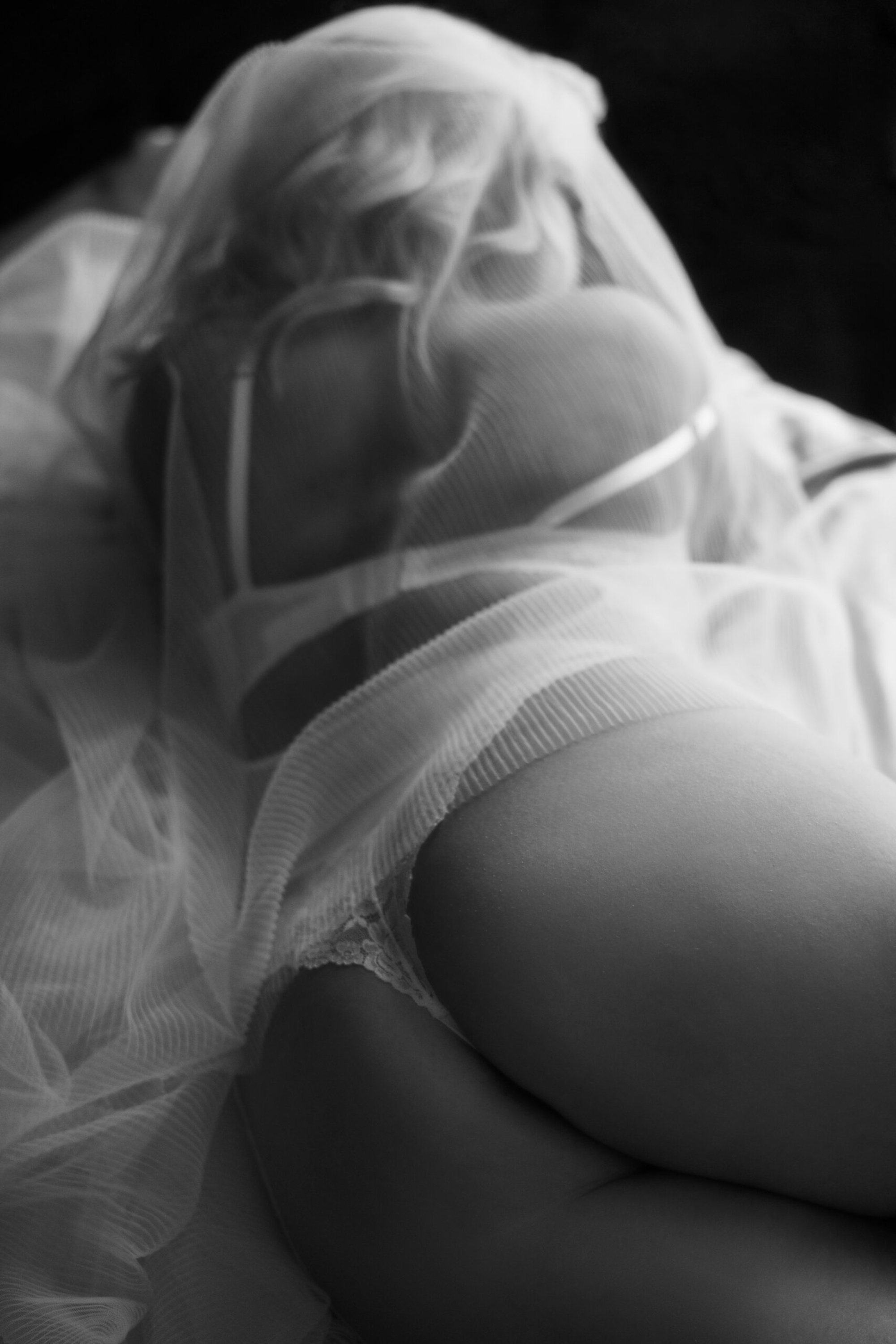 Black and white intimate bridal boudoir photo of a woman in lingerie draped in a sheer veil.