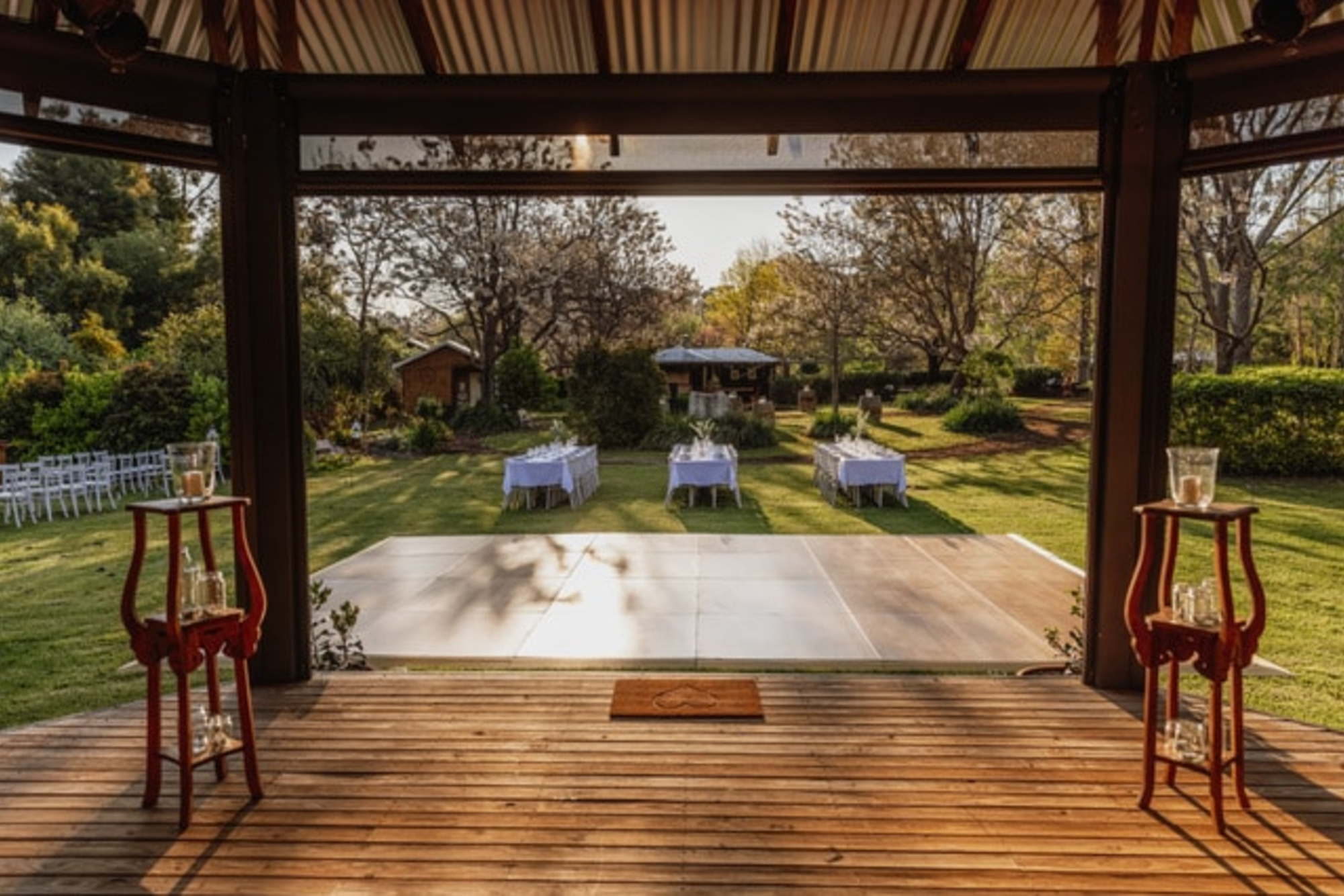 Rustic outdoor wedding venue with a covered deck overlooking a lawn dance floor and gazebo setup.