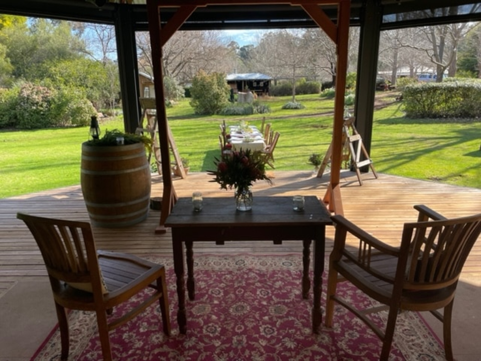 Rustic outdoor wedding ceremony setup with wooden chairs, floral centerpiece, and garden views.