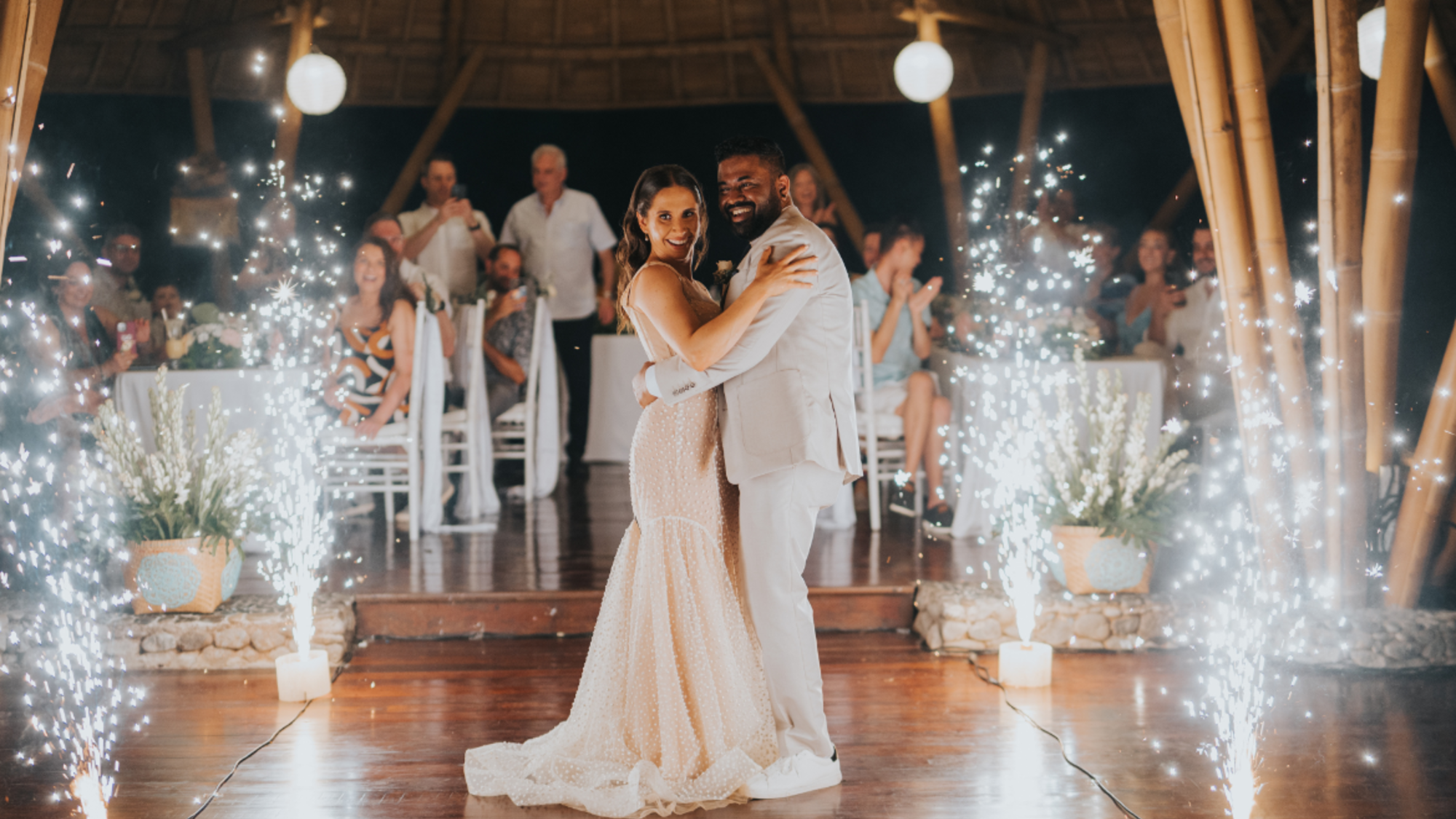 Bride and groom share their first dance surrounded by indoor sparklers at a tropical evening wedding reception.