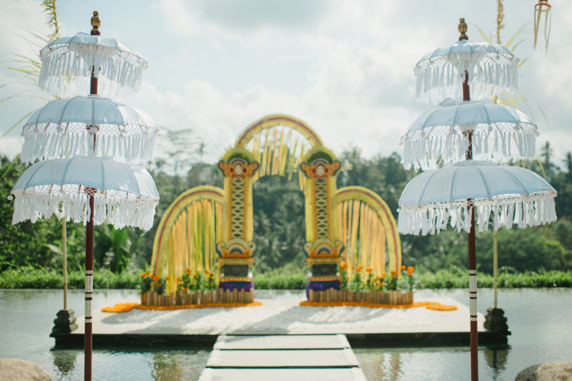 Colorful tropical wedding ceremony arch over water framed by white tiered parasols.