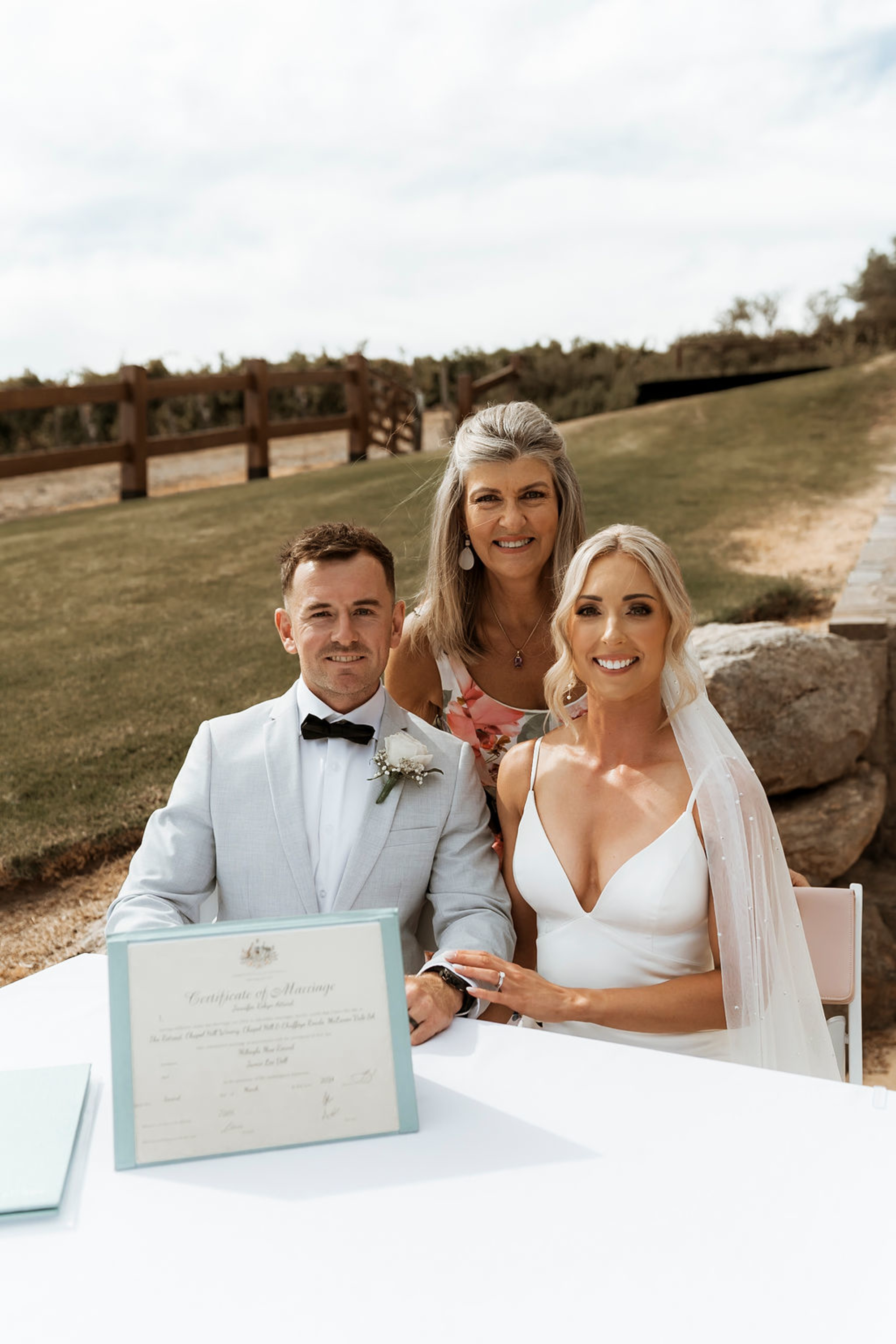 Bride and groom sign their marriage certificate outdoors with a celebrant standing behind them.