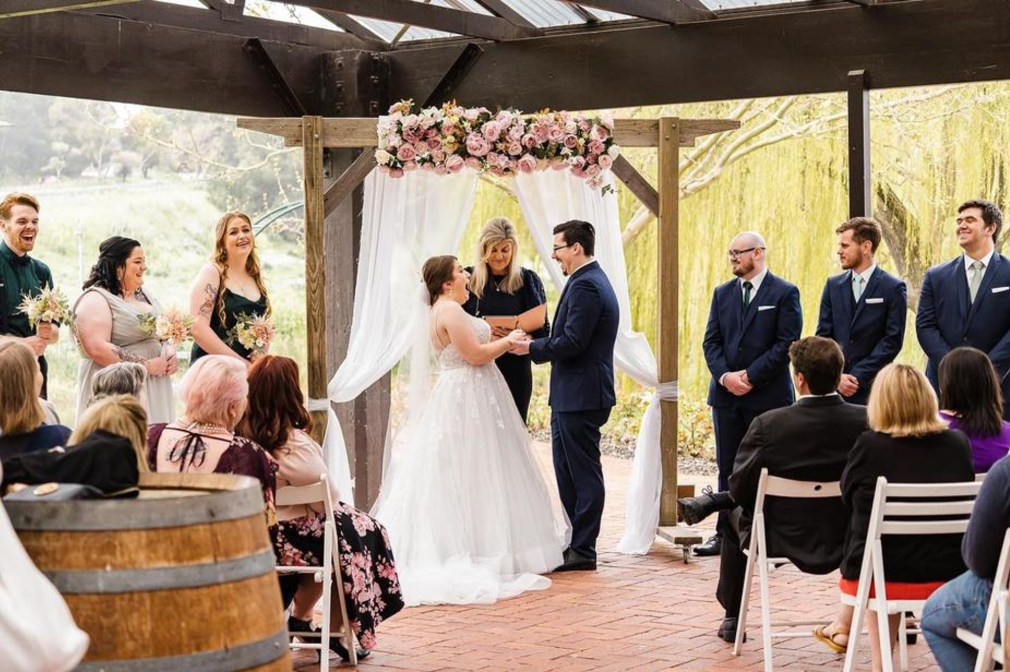 Outdoor wedding ceremony under a floral arch with the couple exchanging vows before seated guests.