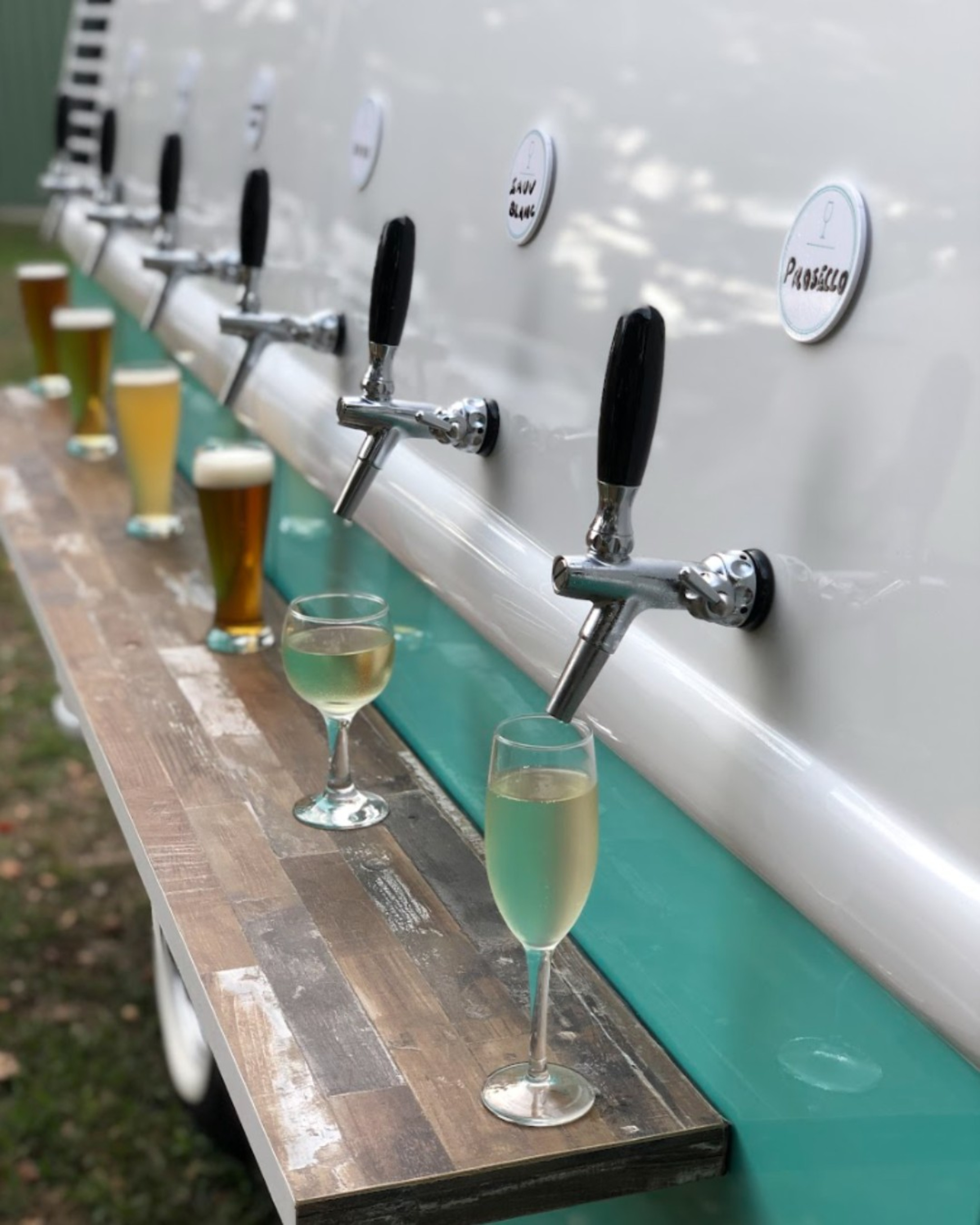 Close-up of a mobile wedding bar with beer and prosecco taps pouring drinks into glasses on a wooden counter.
