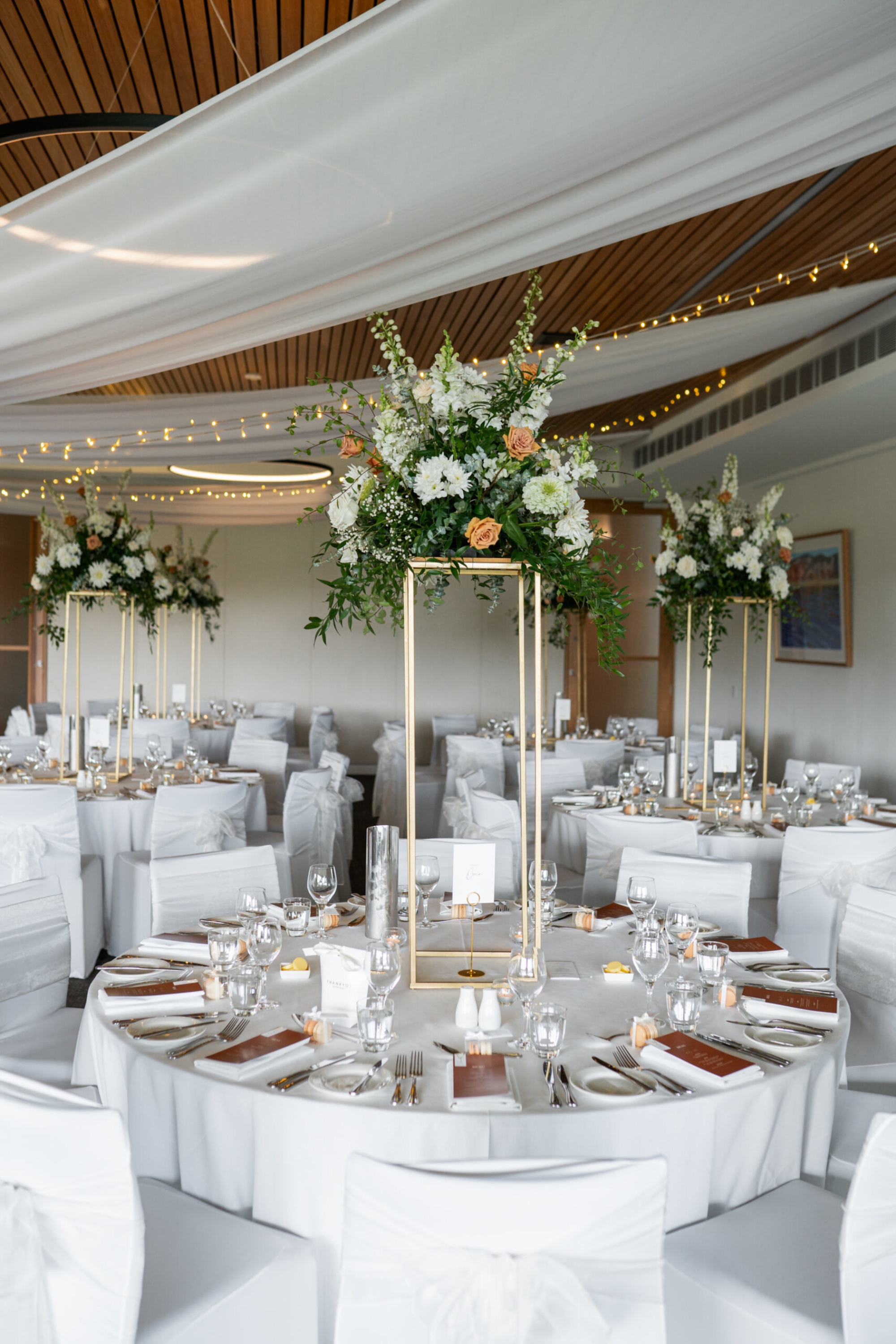 Elegant indoor wedding reception with tall floral centerpieces and white-draped round tables.