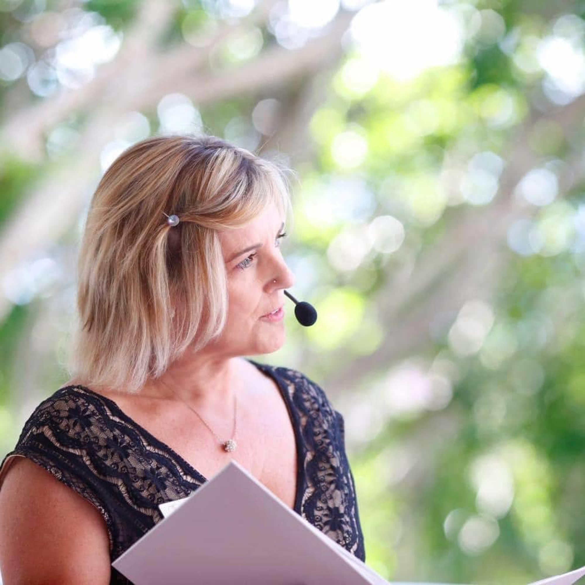 Female wedding celebrant with microphone holding ceremony script outdoors.