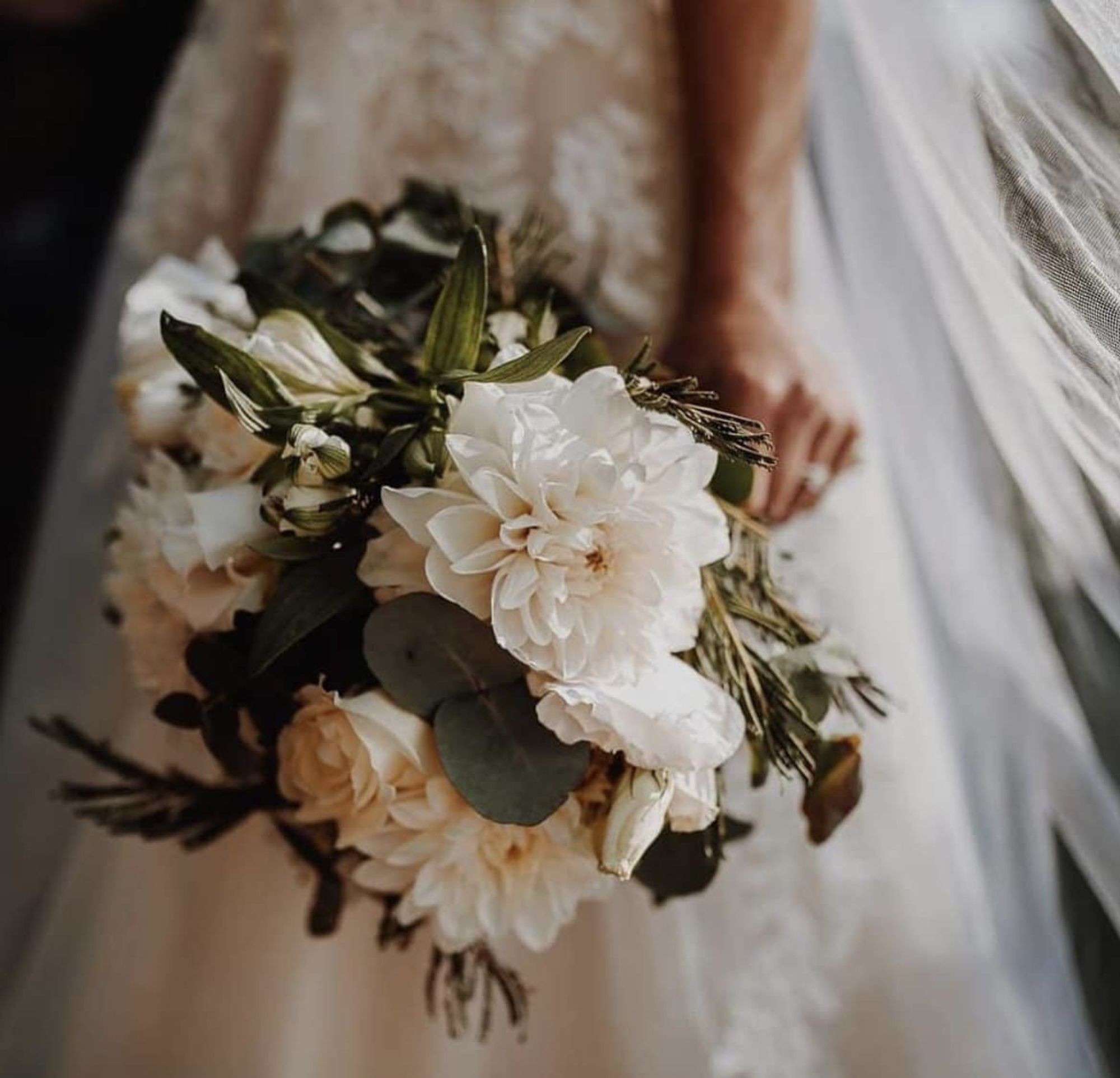 Bride holding a lush white and green bouquet with soft blooms and foliage.