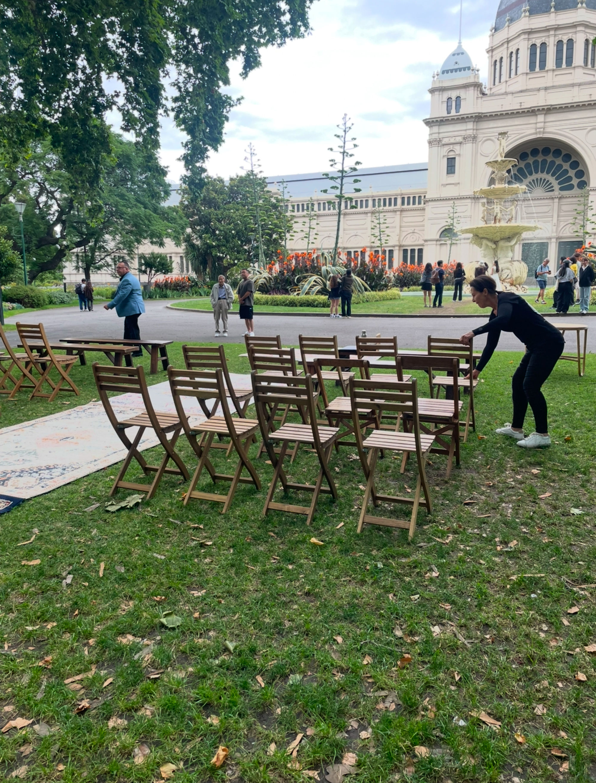 Coordinator arranges wooden chairs for an outdoor wedding ceremony in front of a historic building and fountain.