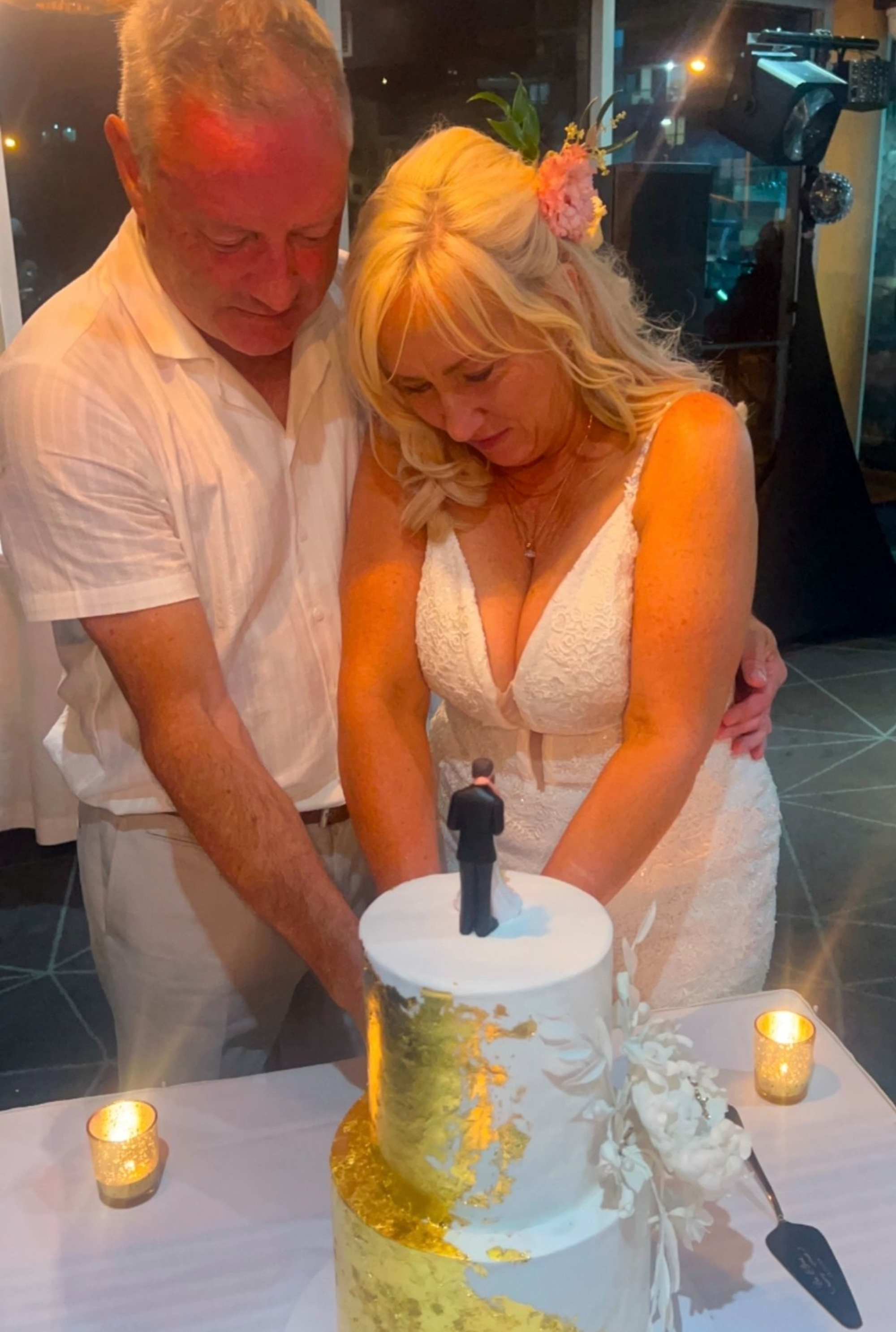 Bride and groom cutting a white and gold wedding cake together at their evening reception.