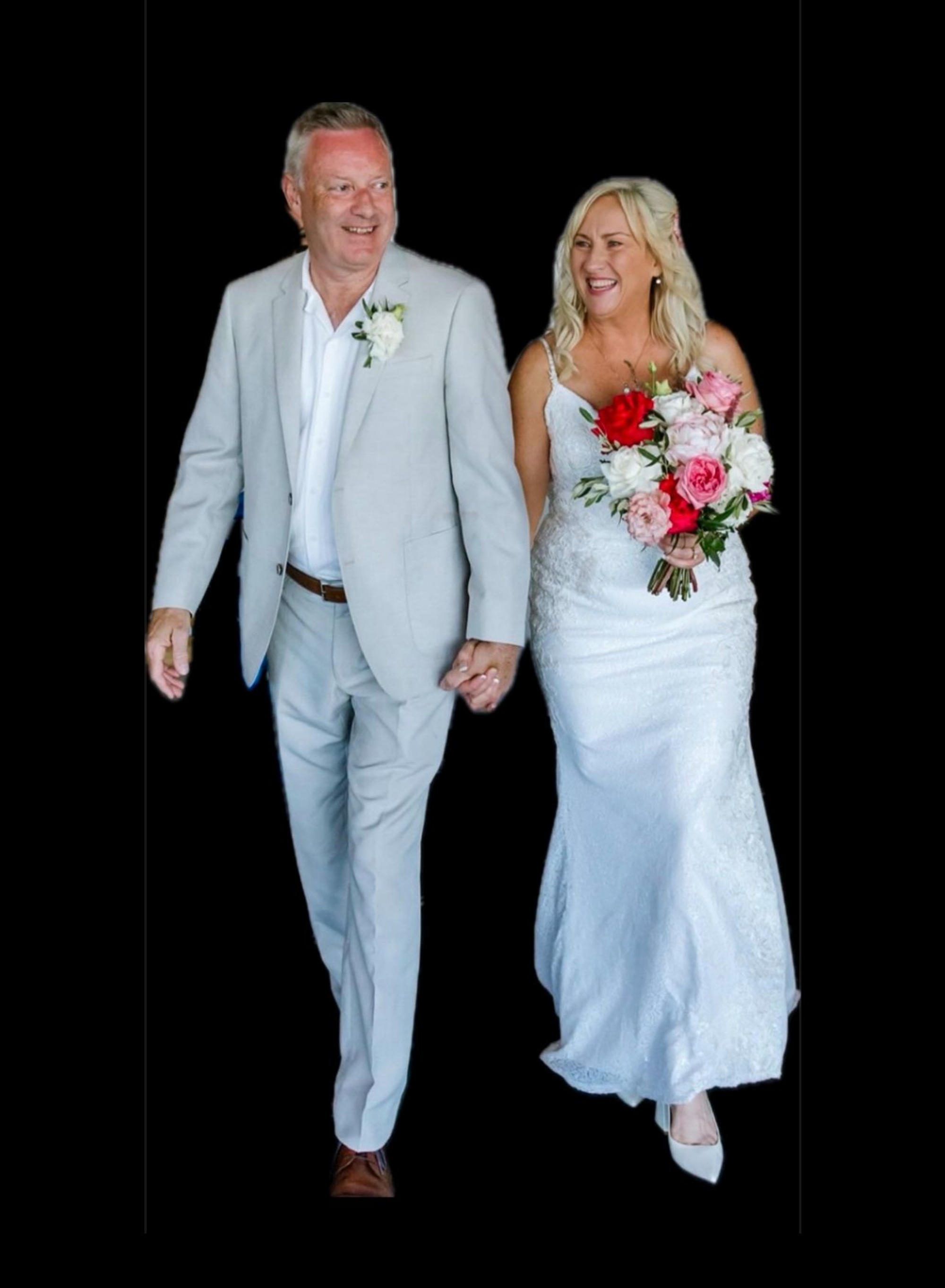 Smiling bride and groom holding hands and walking together, with the bride carrying a colorful bouquet against a black background.