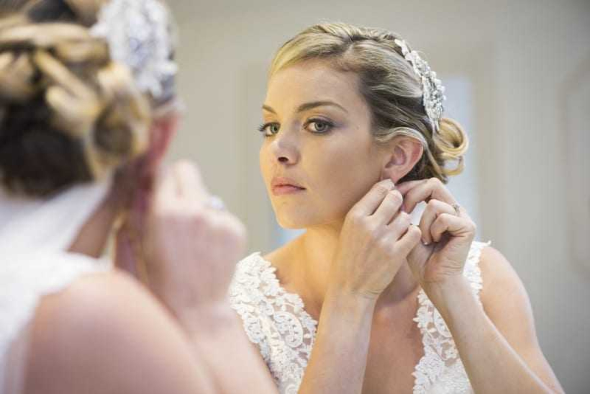 Bride adjusts her earring in front of a mirror while getting ready on her wedding day.