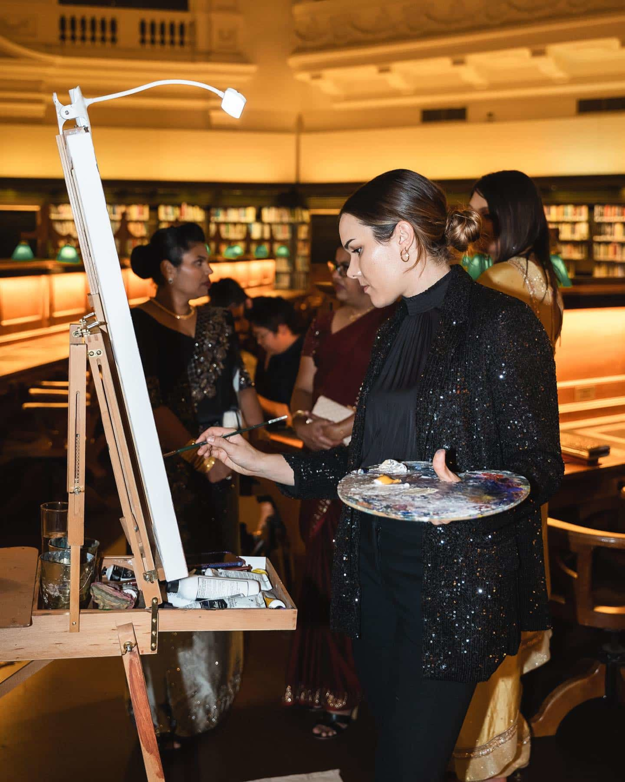 Live event painter creates a wedding scene on canvas during an elegant indoor reception with guests watching.