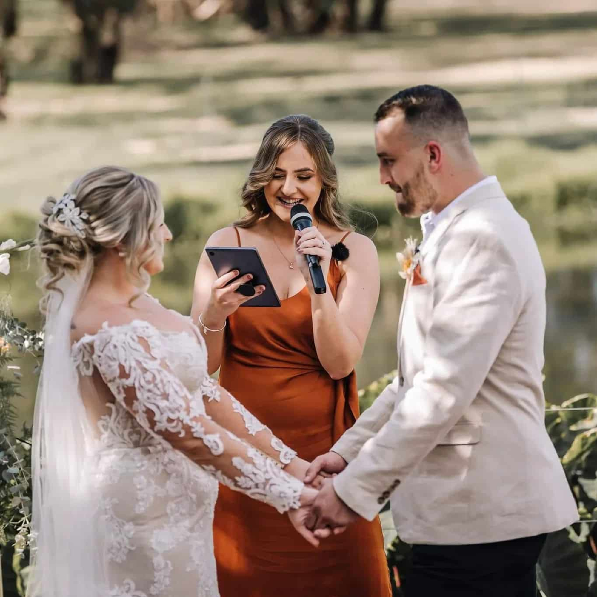 Outdoor wedding ceremony with a celebrant reading vows as the couple holds hands.
