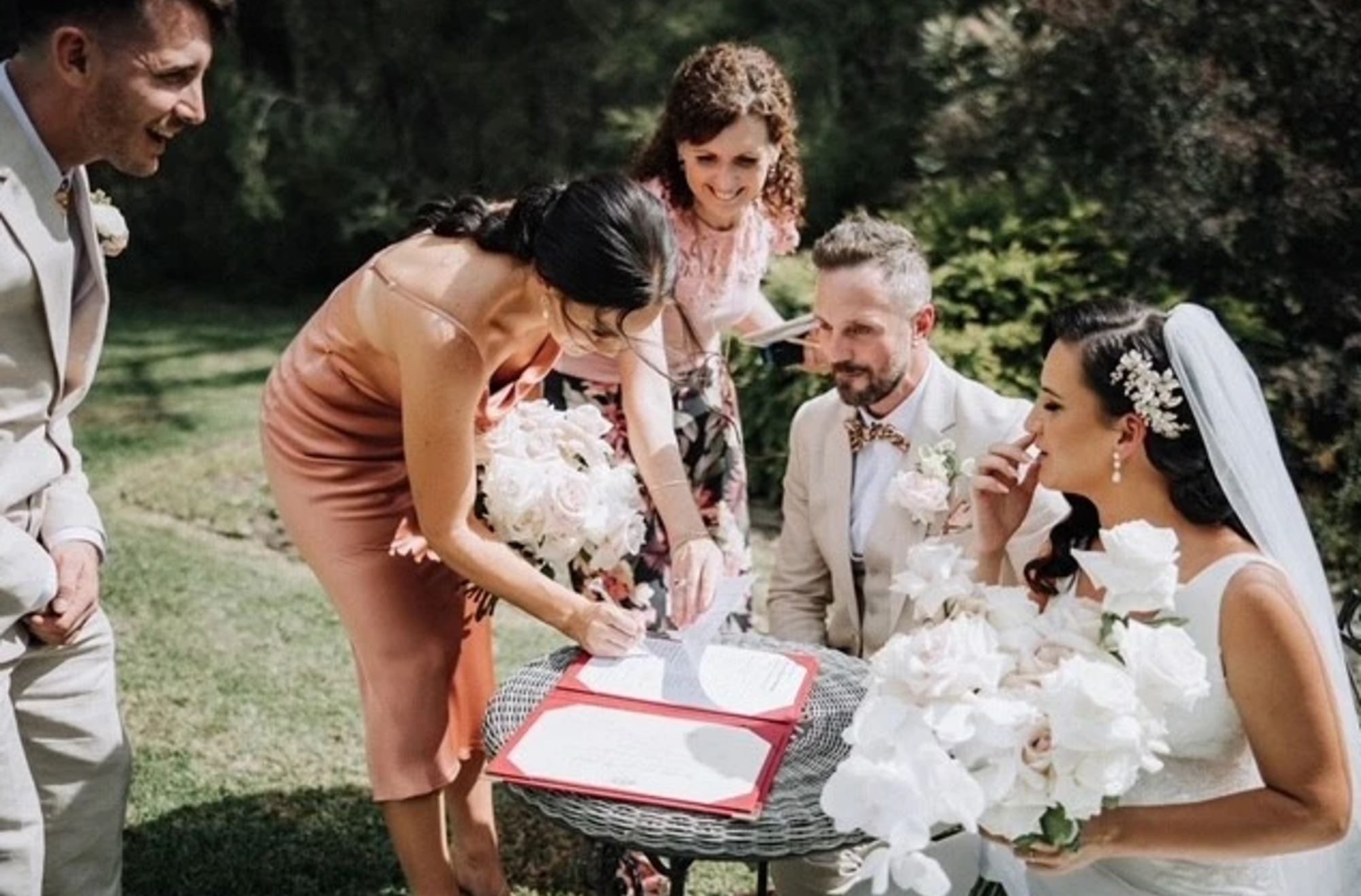 Bride, groom and witnesses sign the marriage registry at an outdoor garden wedding.
