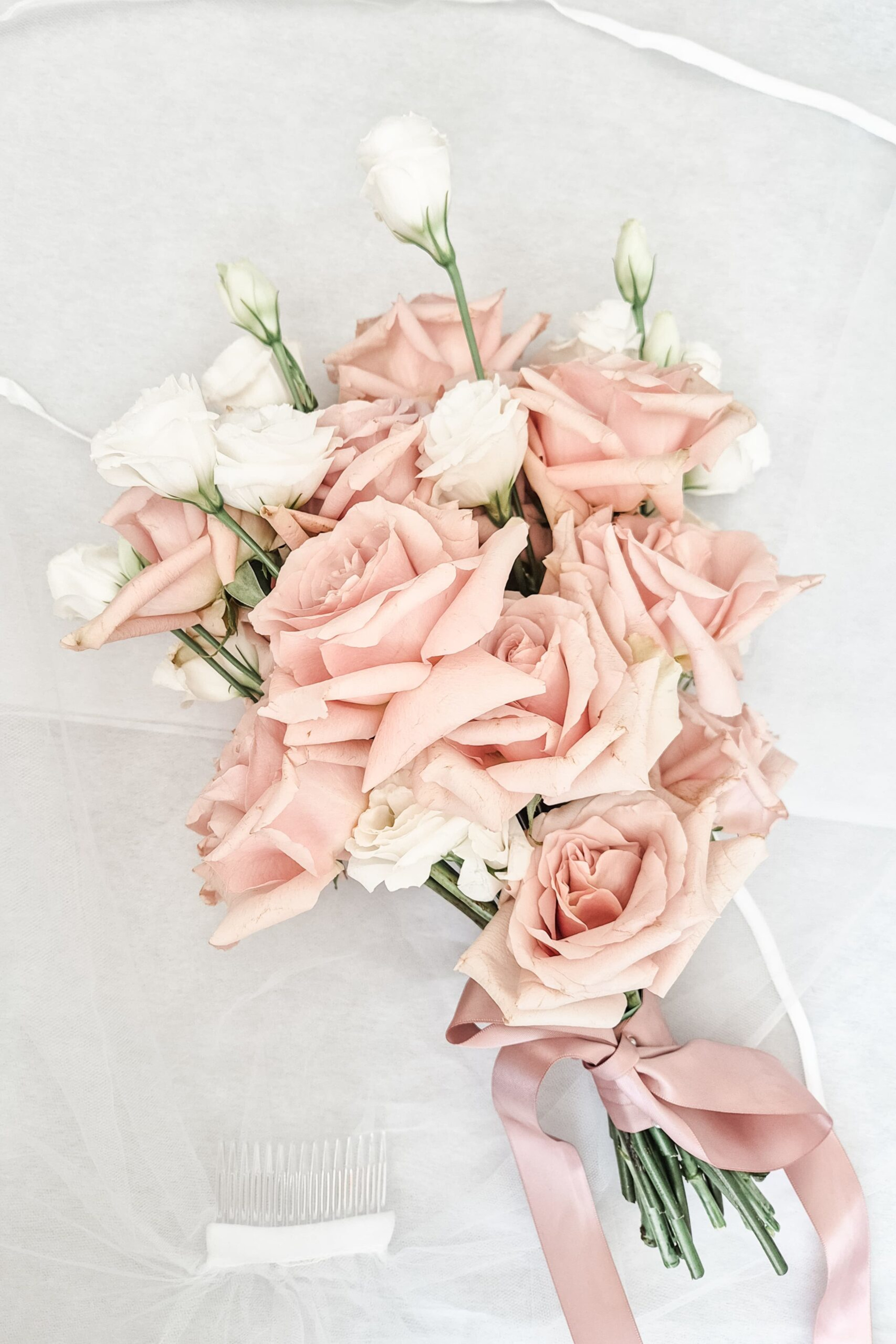 Blush pink and white rose bridal bouquet with satin ribbon laid on soft tulle fabric.