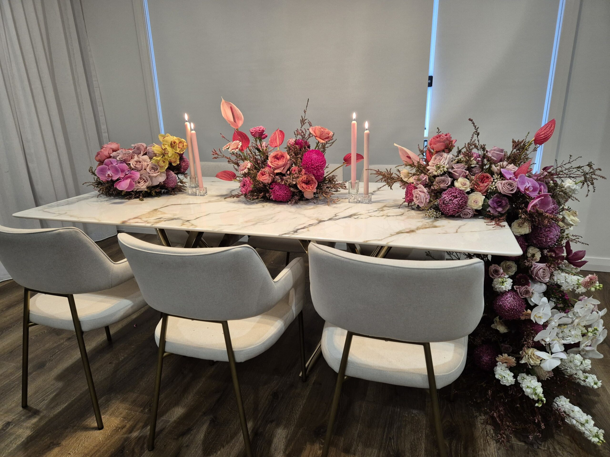 Modern marble wedding table styled with pink floral arrangements and taper candles surrounded by upholstered chairs.