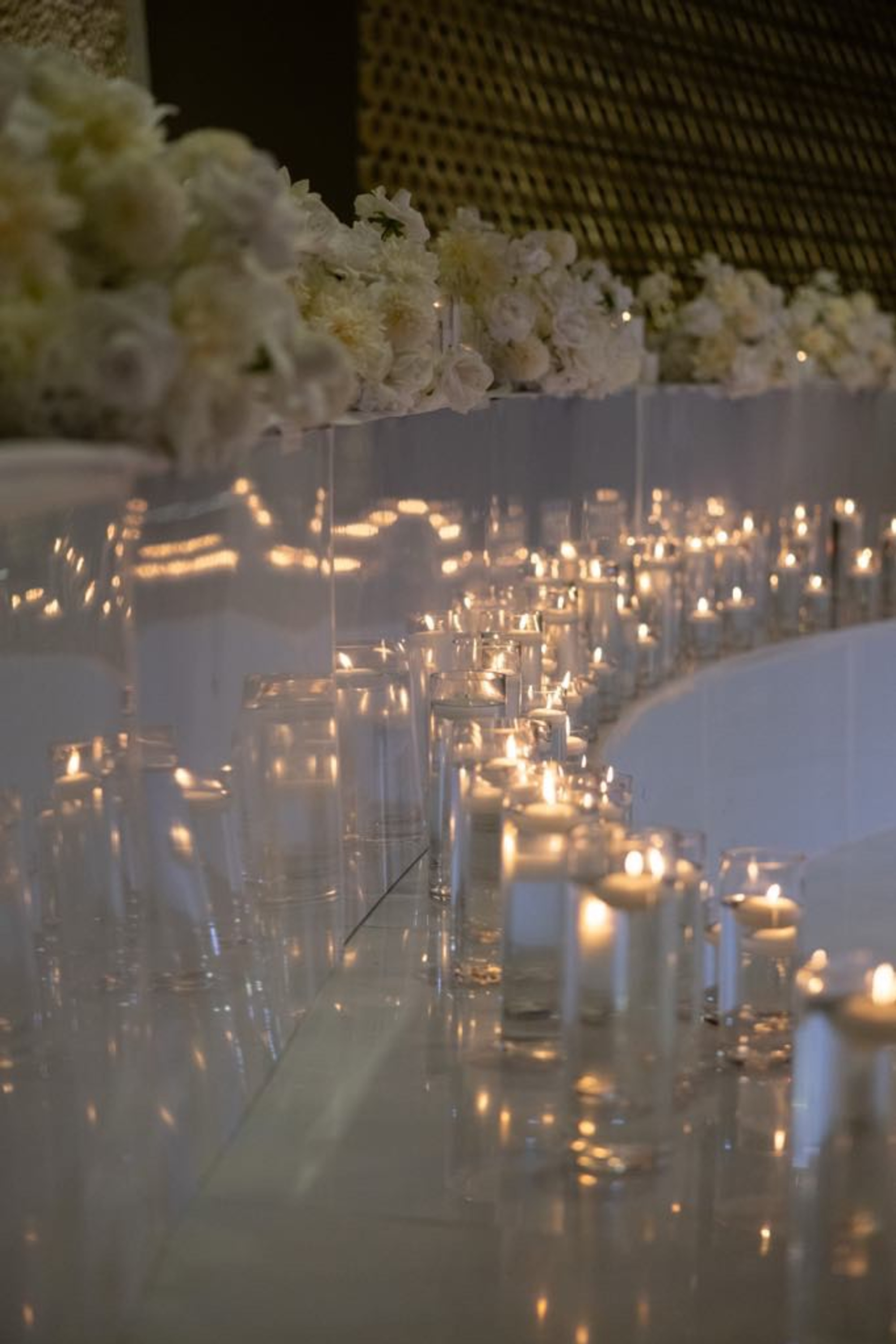 Elegant wedding aisle lined with floating candles in glass vases and white floral arrangements.