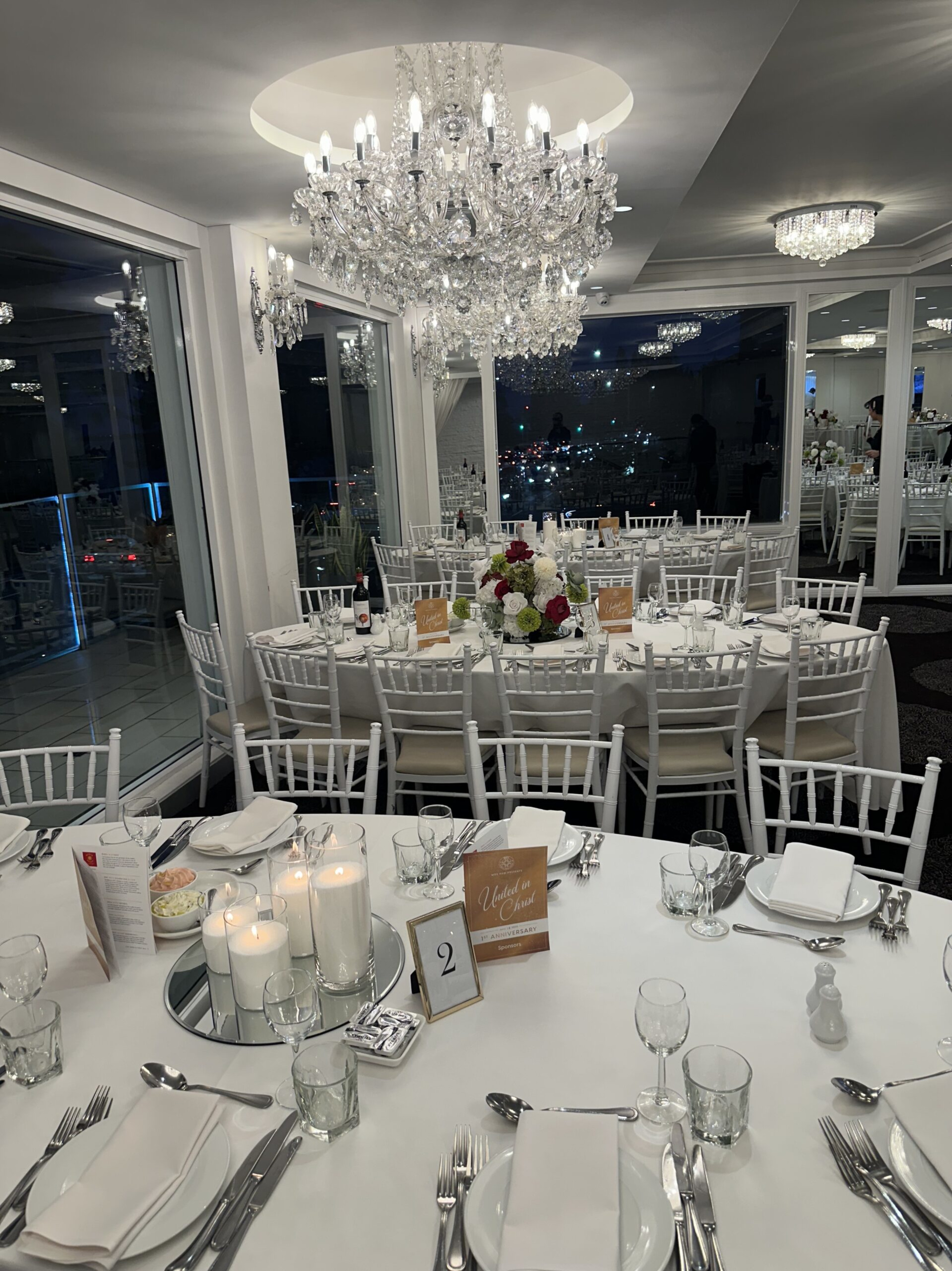 Elegant indoor wedding reception venue with crystal chandeliers and white table settings around round banquet tables.