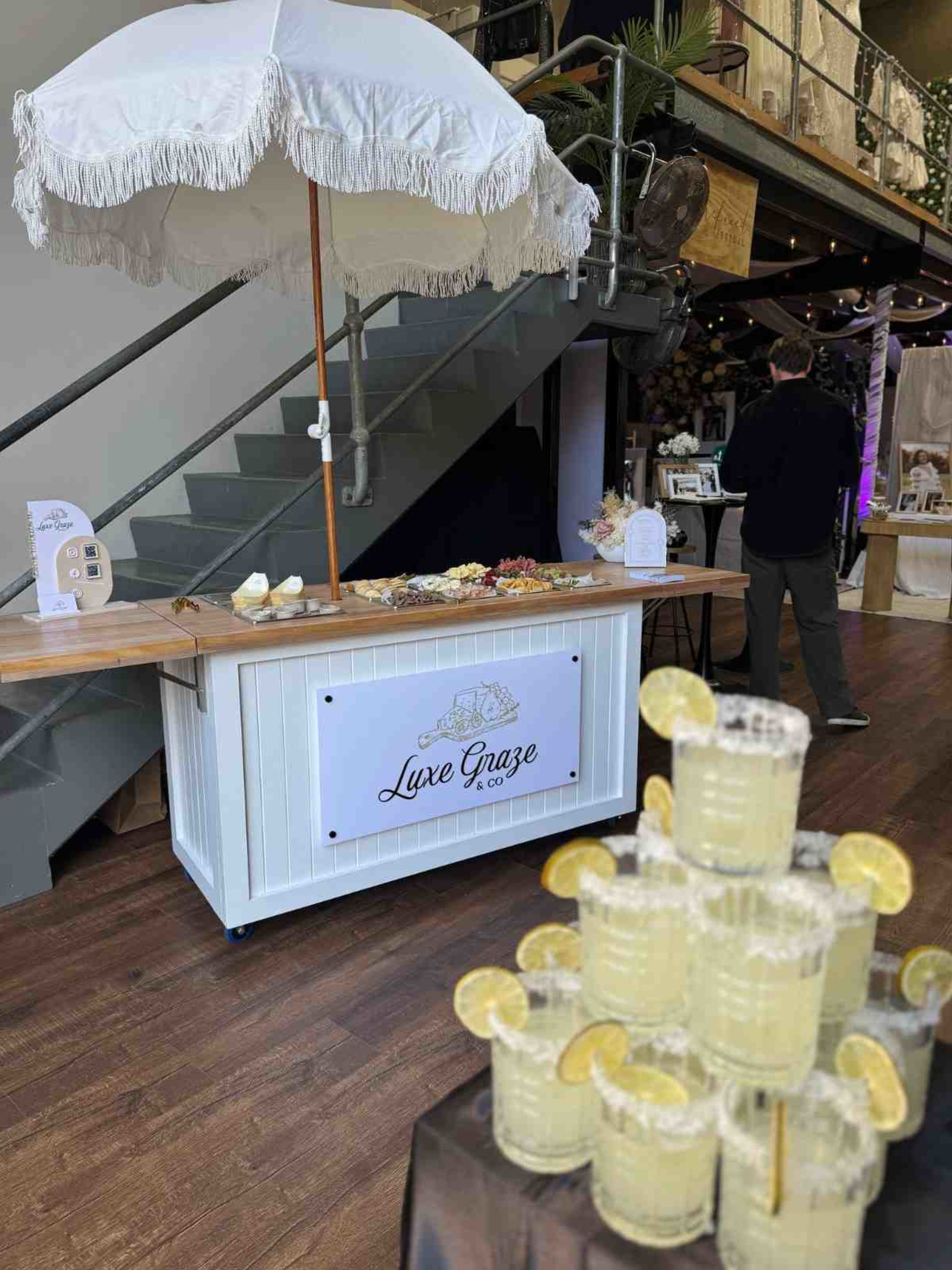 Indoor wedding grazing station with white parasol and a stacked display of lemon cocktails in the foreground.