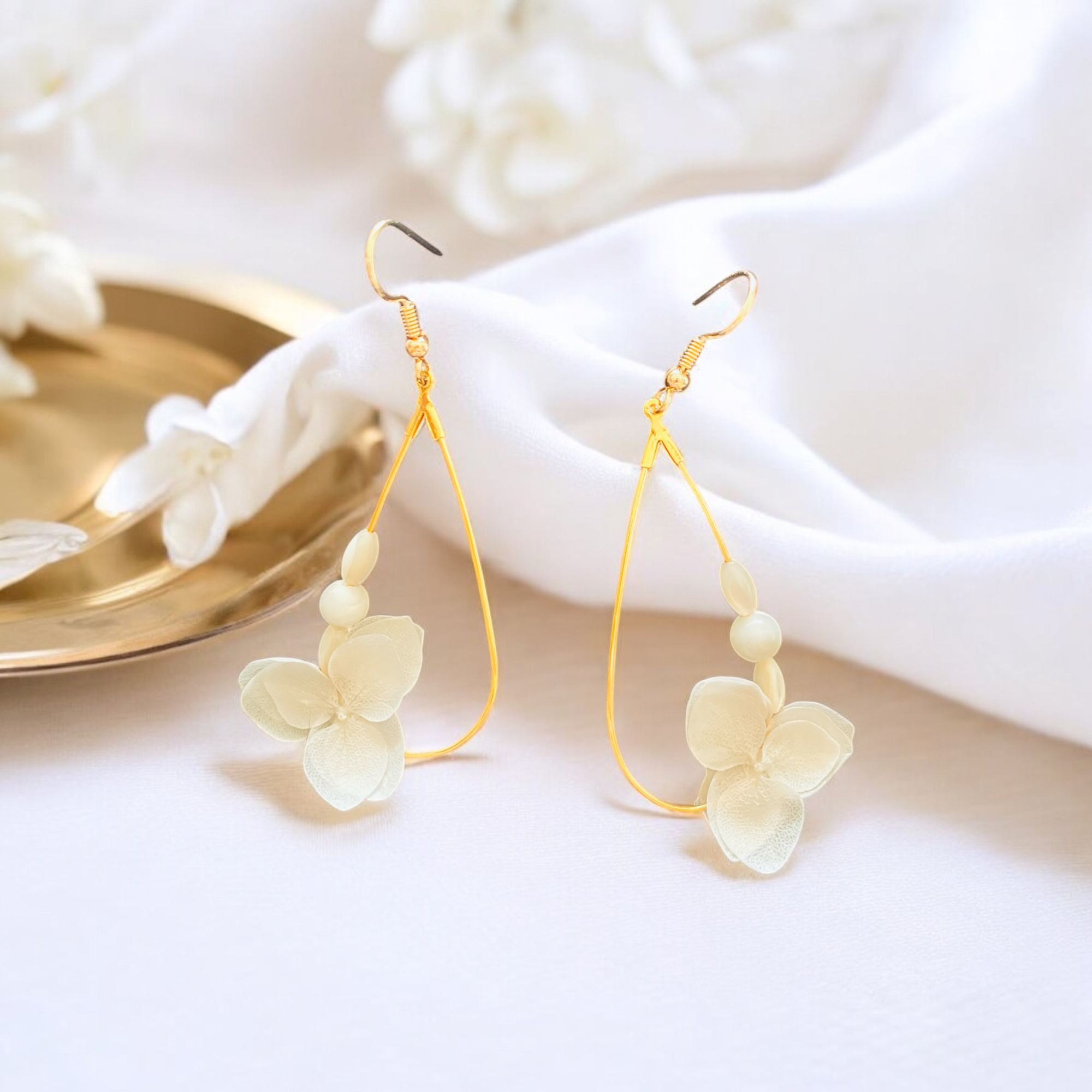 Delicate gold hoop earrings with ivory flower accents displayed on soft white fabric.